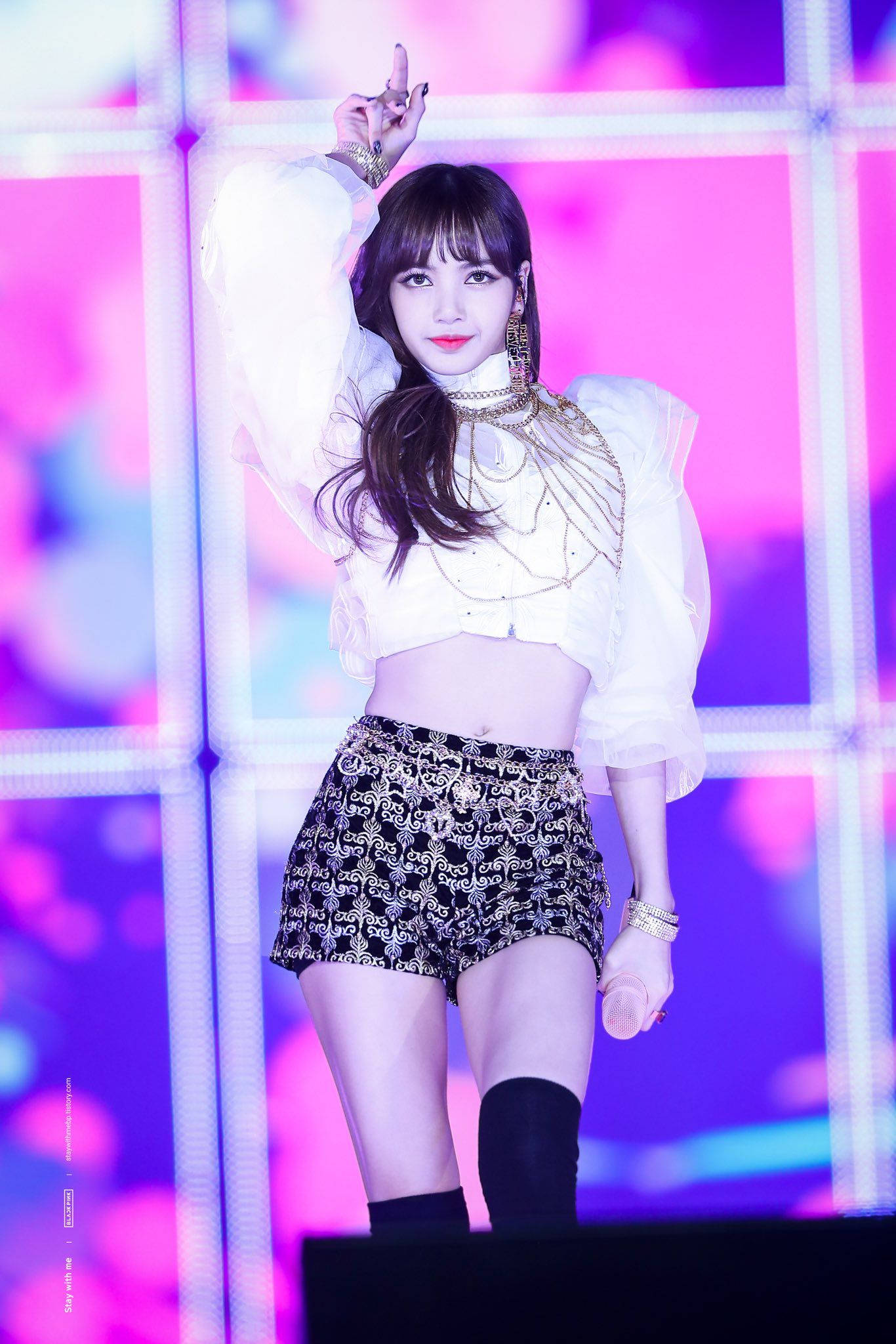 Lalisa 桌布 壁紙 — 一位身穿白色泡泡袖上衣和圖案短褲的女表演者在充滿活力的粉紅色和紫色燈光舞台上擺姿勢。