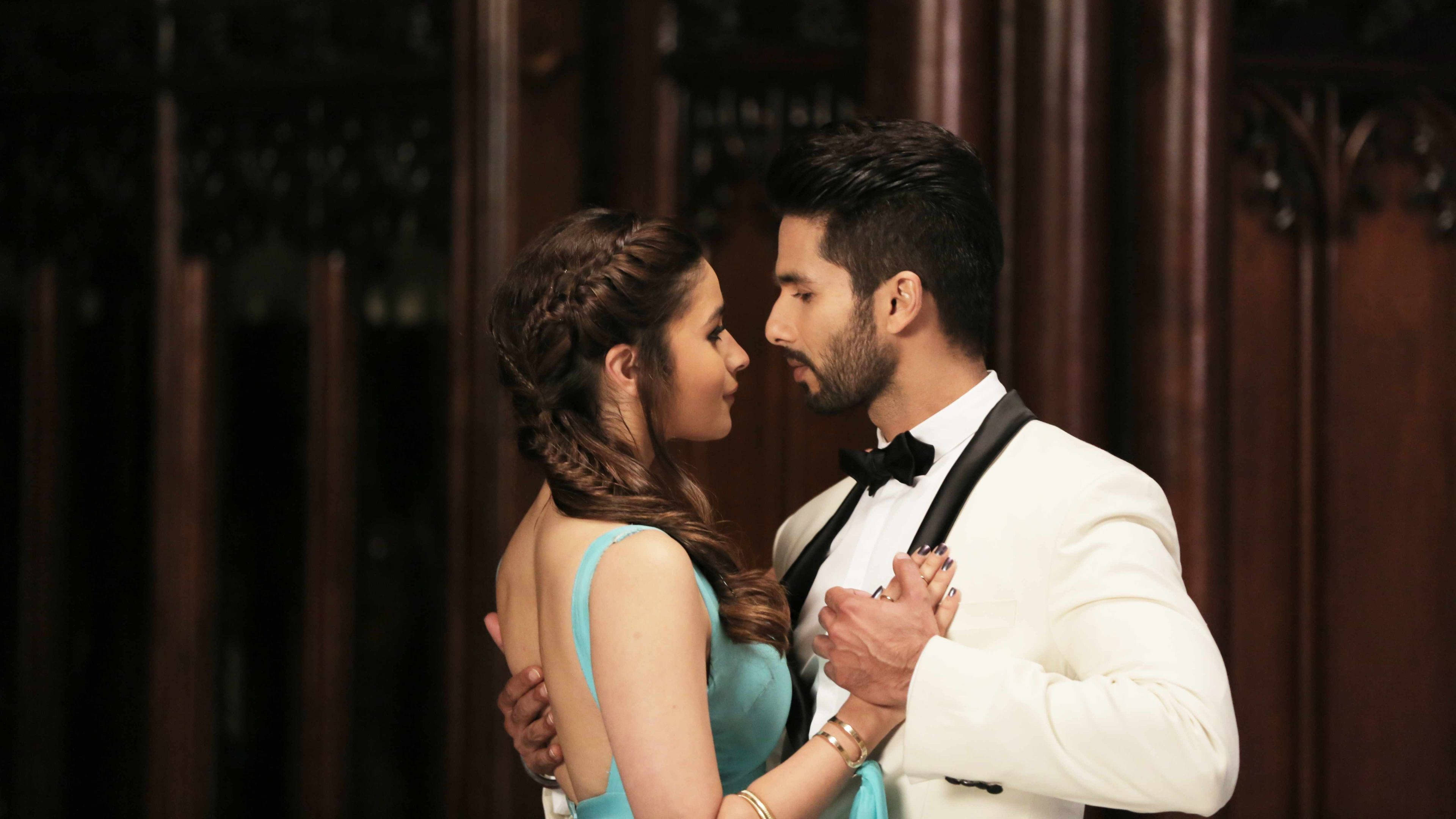 Shahid Kapoor 桌布 壁紙 — 一位身穿白色燕尾服的男士和一位身穿藍色連衣裙的女士在深色木鑲板牆前深情對望。