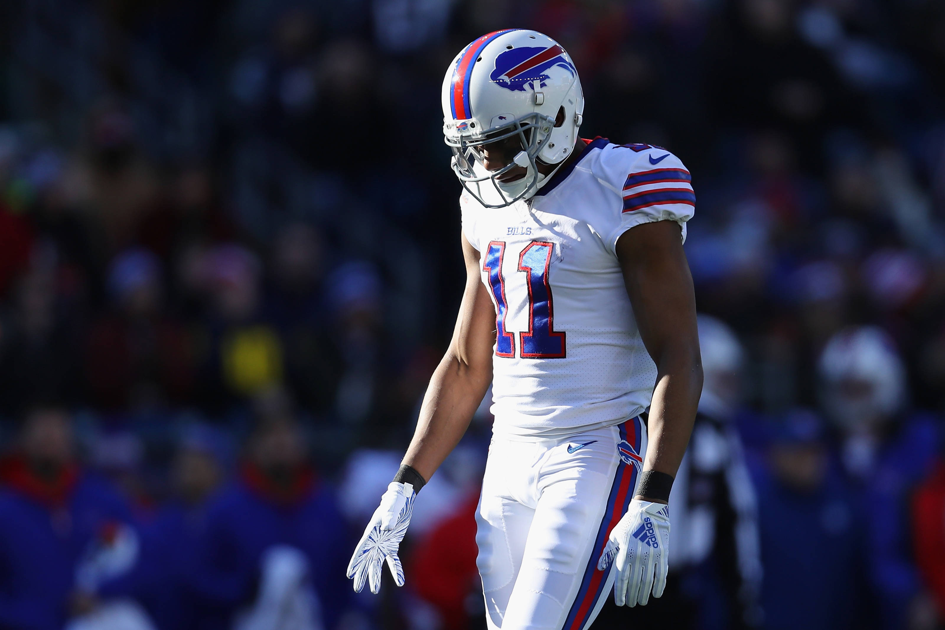 zay jones 桌布 壁紙 — 一位身穿白色球衣、背號11號的布法羅比爾隊美式足球員，在明亮的日光下走進球場，背景是模糊的人群。