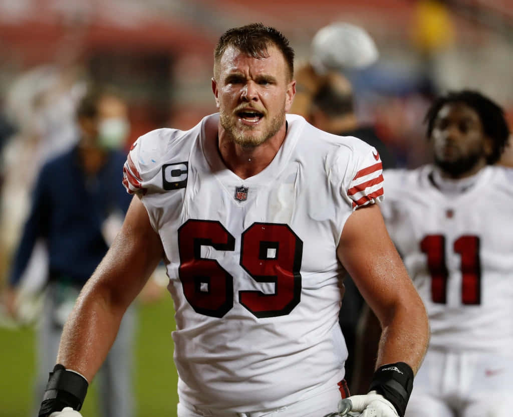 Mike Mcglinchey 桌布 壁紙 — 一位身穿白色球衣、號碼69的堅定NFL球員在夜間比賽中於球場燈光下激烈咆哮。