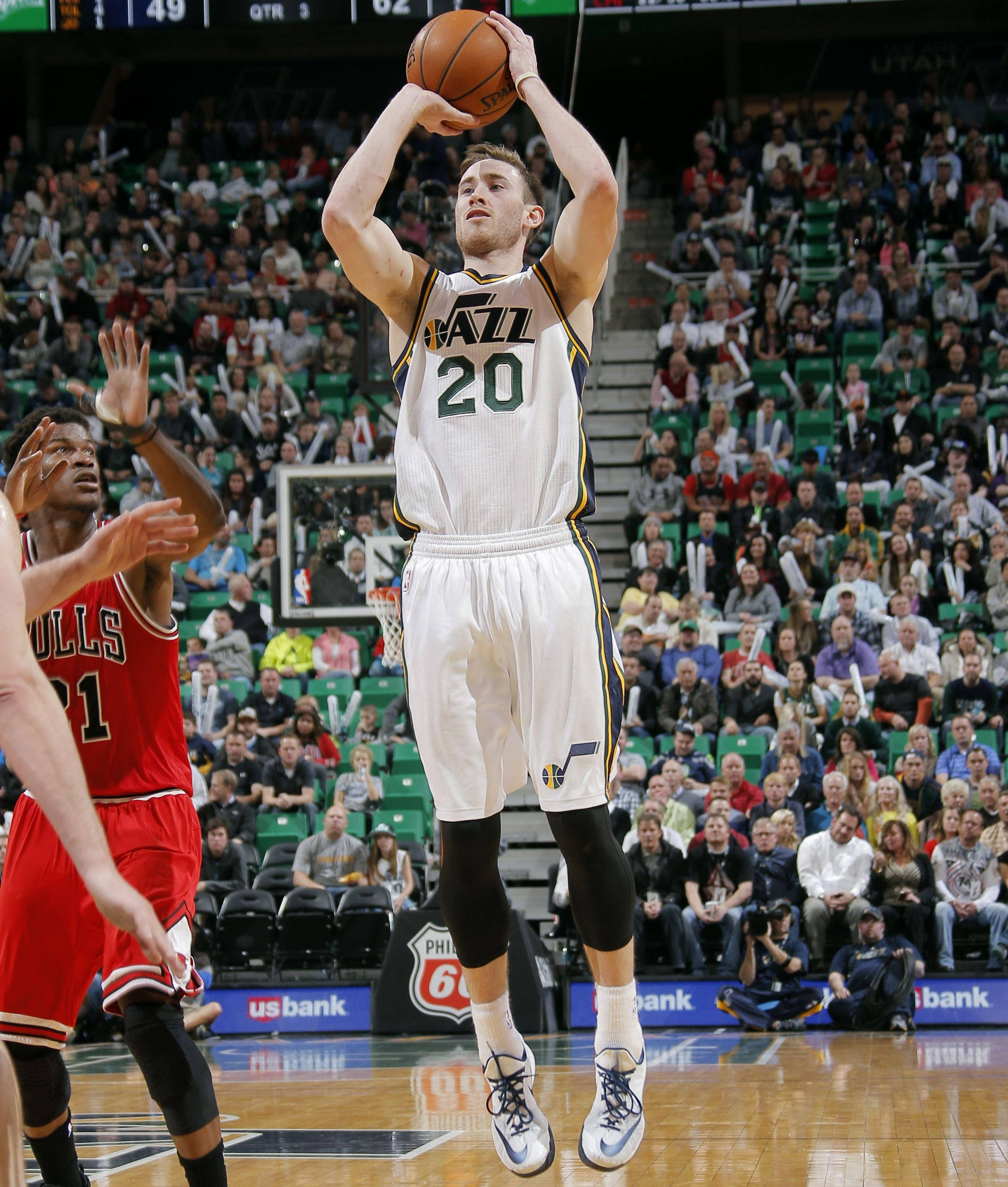 gordon hayward 桌布 壁紙 — 一位身穿白色球衣20號的猶他爵士球員跳起投籃，而芝加哥公牛隊的防守球員在擠滿觀眾的球場比賽中舉手防守。