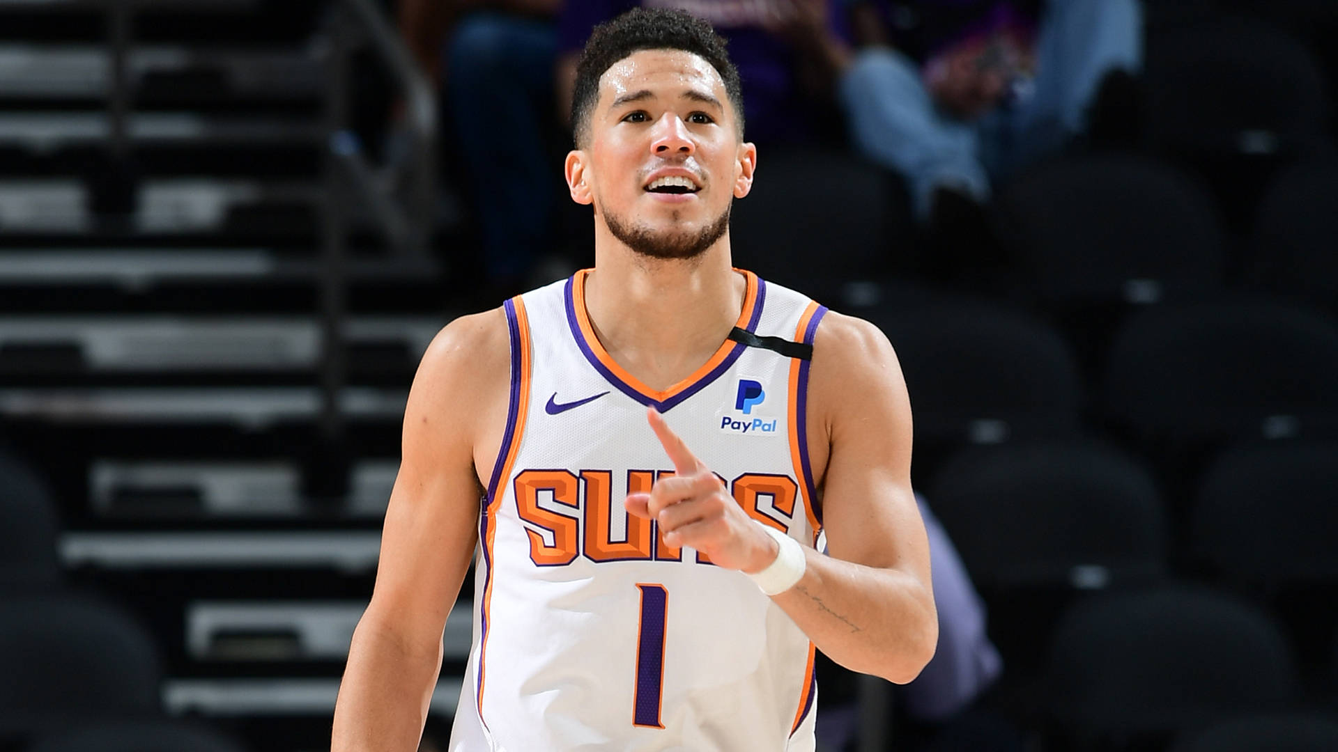 Devin Booker 桌布 壁紙 — 一位身穿白色球衣一號的鳳凰城太陽隊籃球運動員在比賽中專注地向前指。