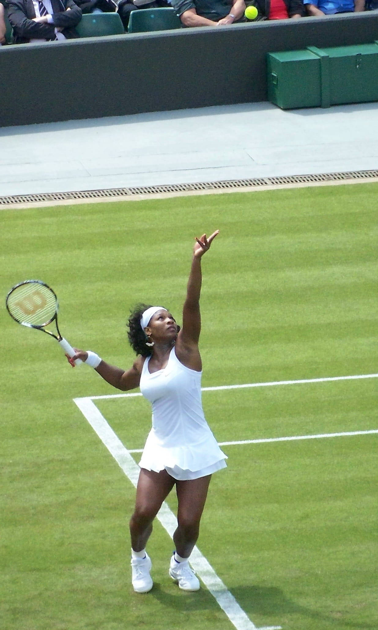 Wimbledon 桌布 壁紙 — 一位身穿白色球衣的女網球選手在草地場上發球，背景有觀眾。