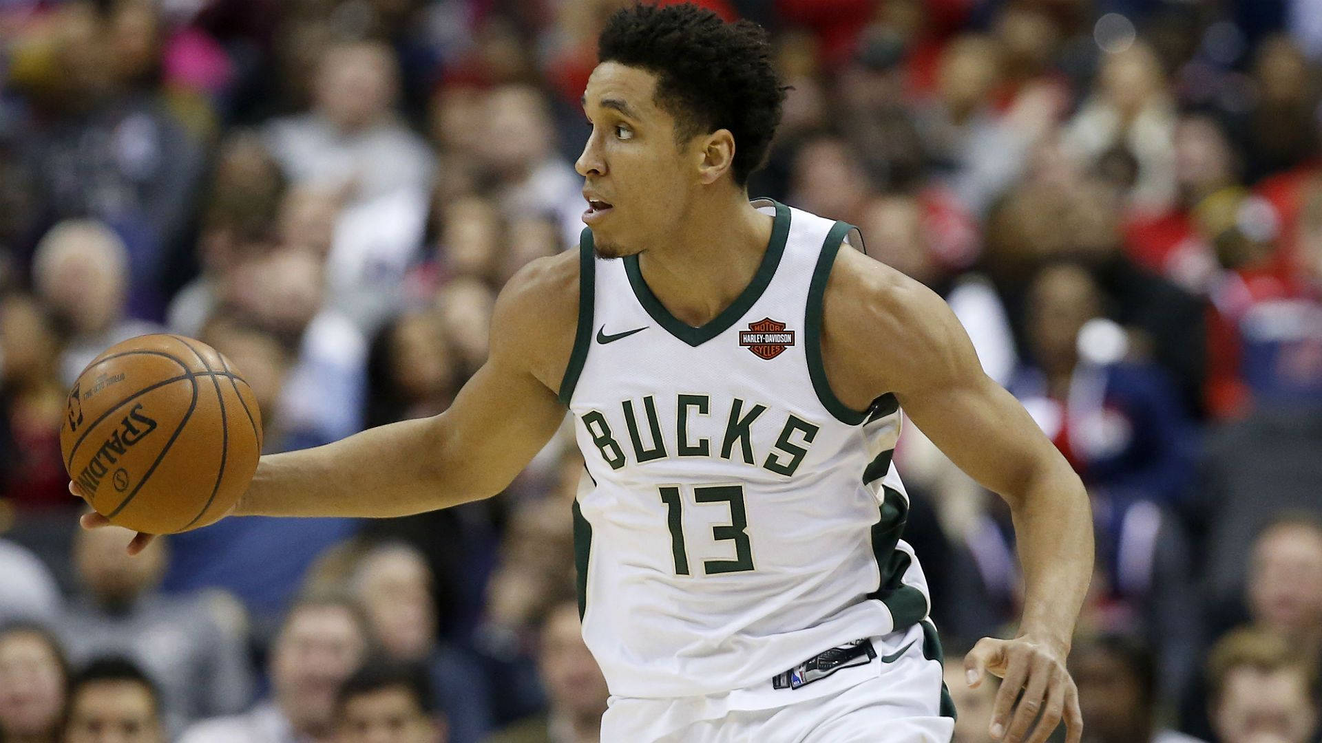 malcolm brogdon 桌布 壁紙 — 一位身穿白色球衣的密爾瓦基公鹿籃球運動員在激烈的比賽中運球，背景是模糊的人群。