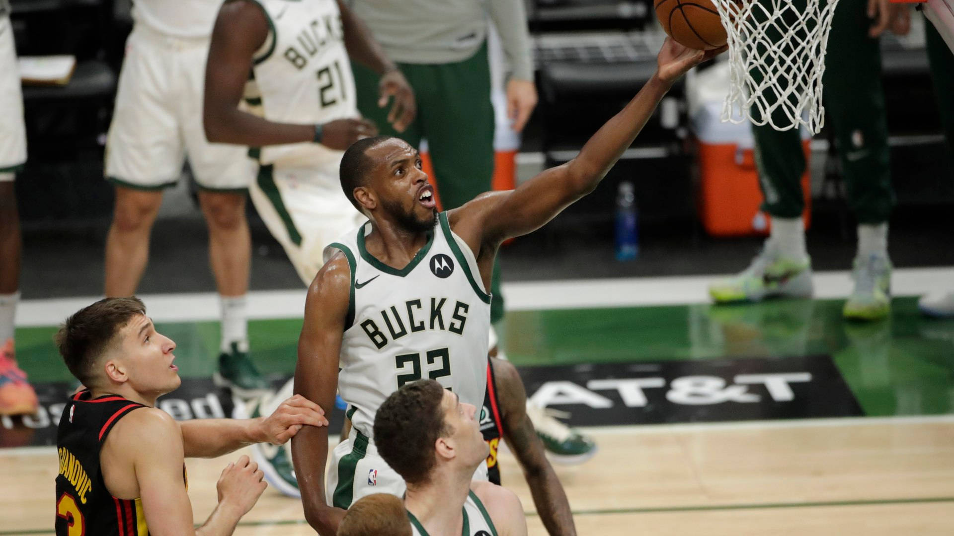 Khris Middleton 桌布 壁紙 — 一位身穿白色球衣的密爾瓦基公鹿隊球員在硬木球場上灌籃，防守球員專注地觀看。