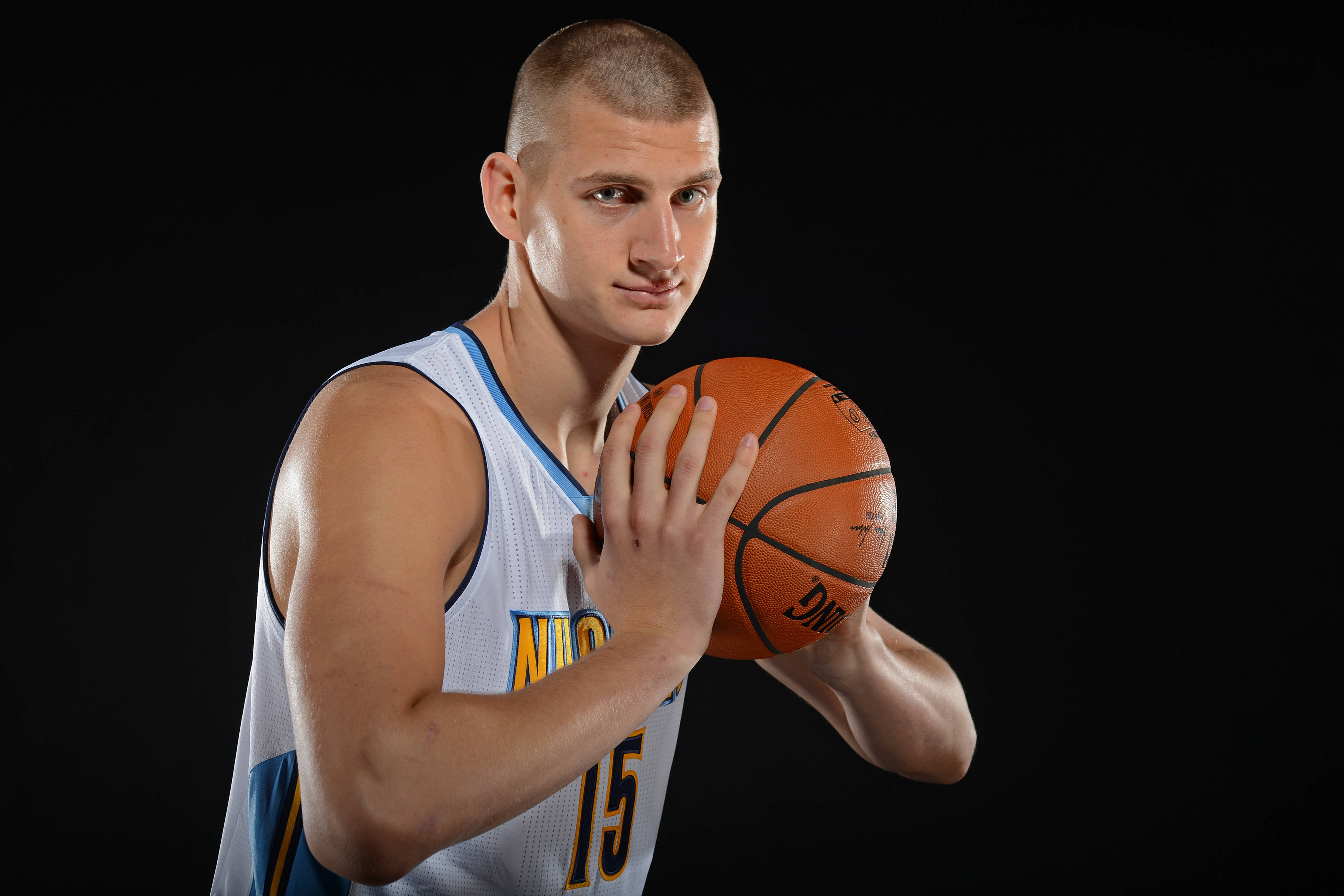 Jokic 桌布 壁紙 — 一位身穿白色球衣的籃球運動員，在黑色背景下專注地拿著一個橙色籃球。