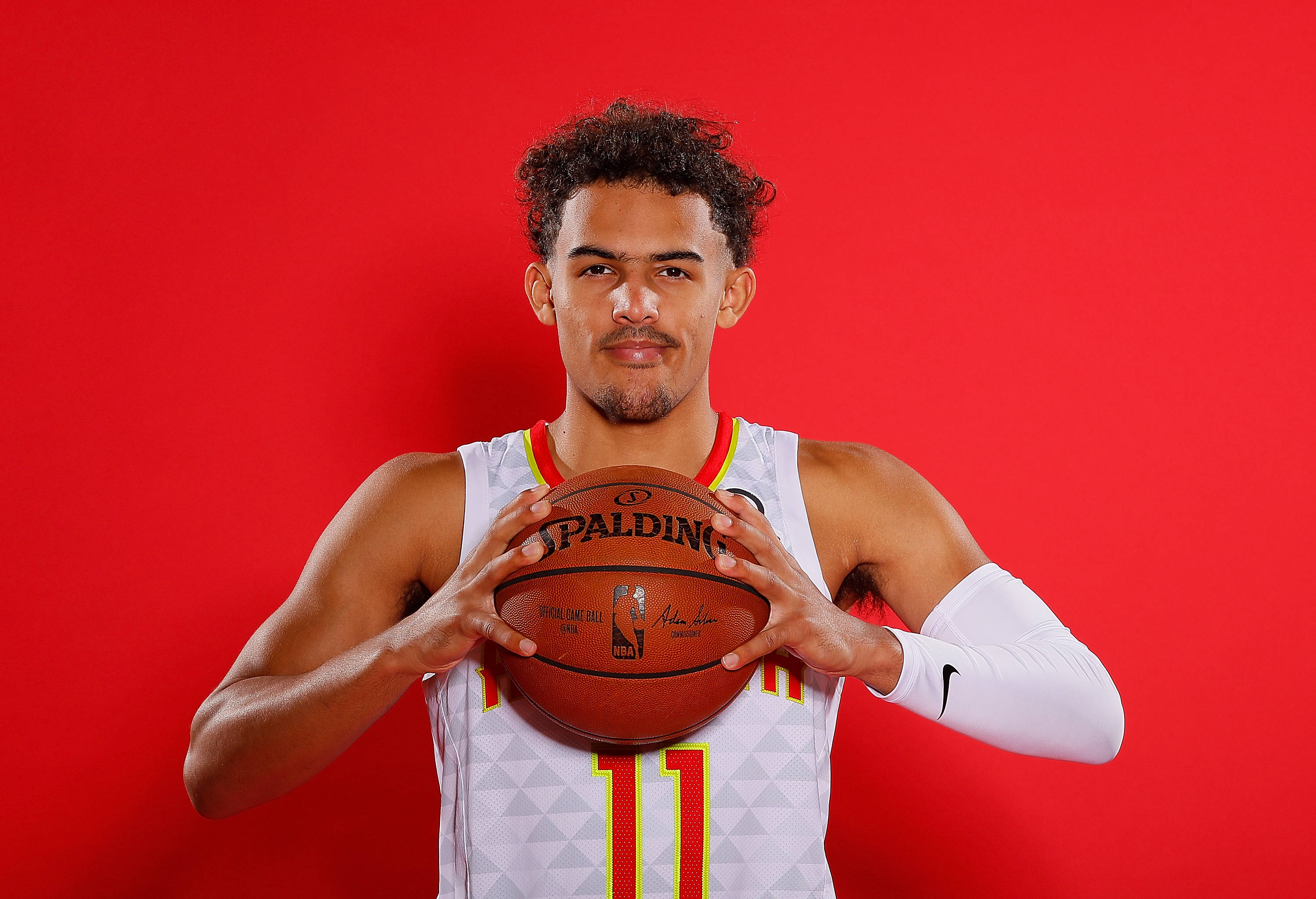 Hawks 桌布 壁紙 — 一位身穿白色球衣的籃球運動員在鮮紅色的攝影棚背景下拿著一個Spalding籃球。