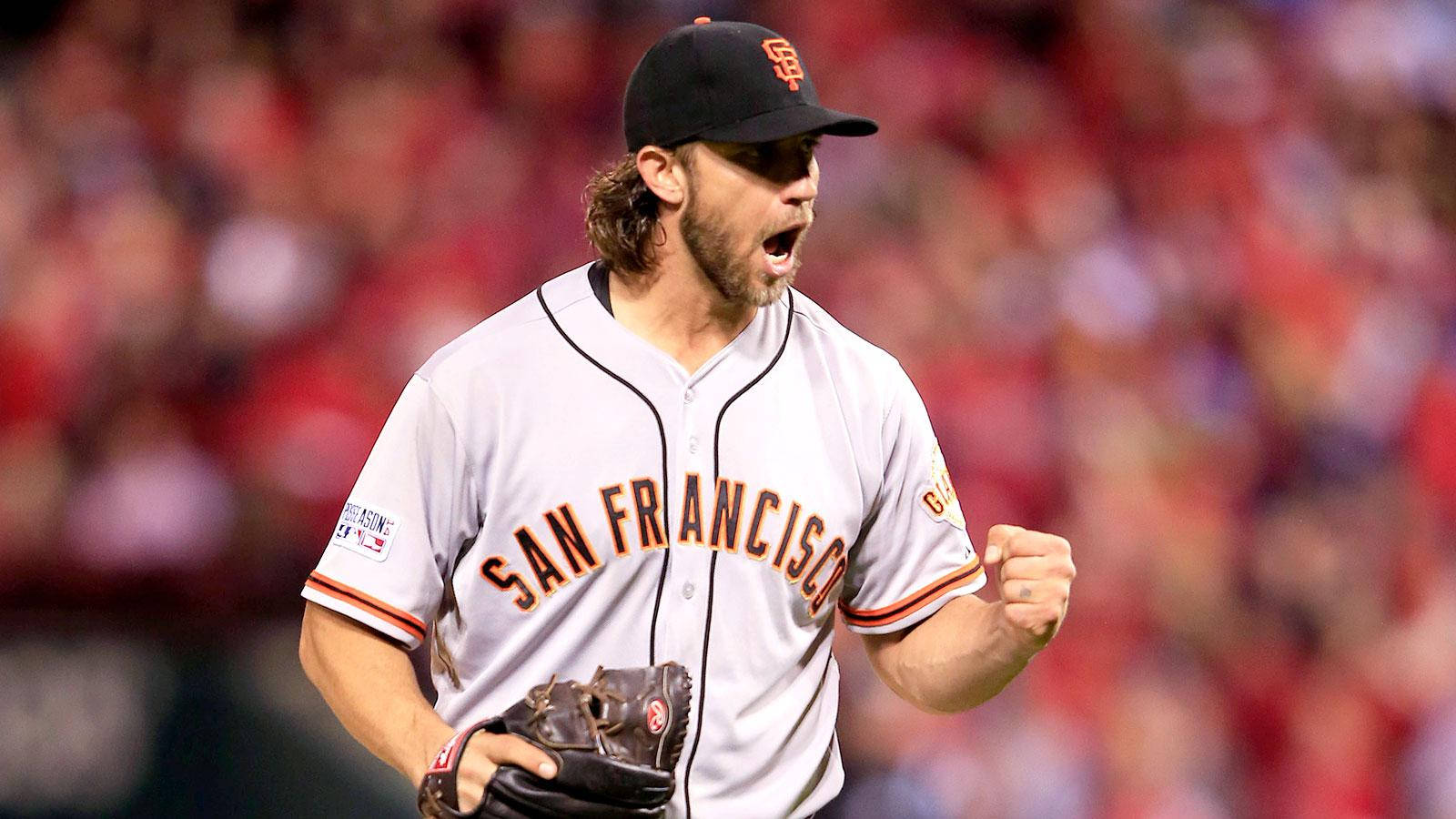 madison bumgarner 桌布 壁紙 — 一位身穿白色球衣的舊金山棒球選手，在模糊的紅色人群前握緊拳頭、張開嘴巴慶祝。