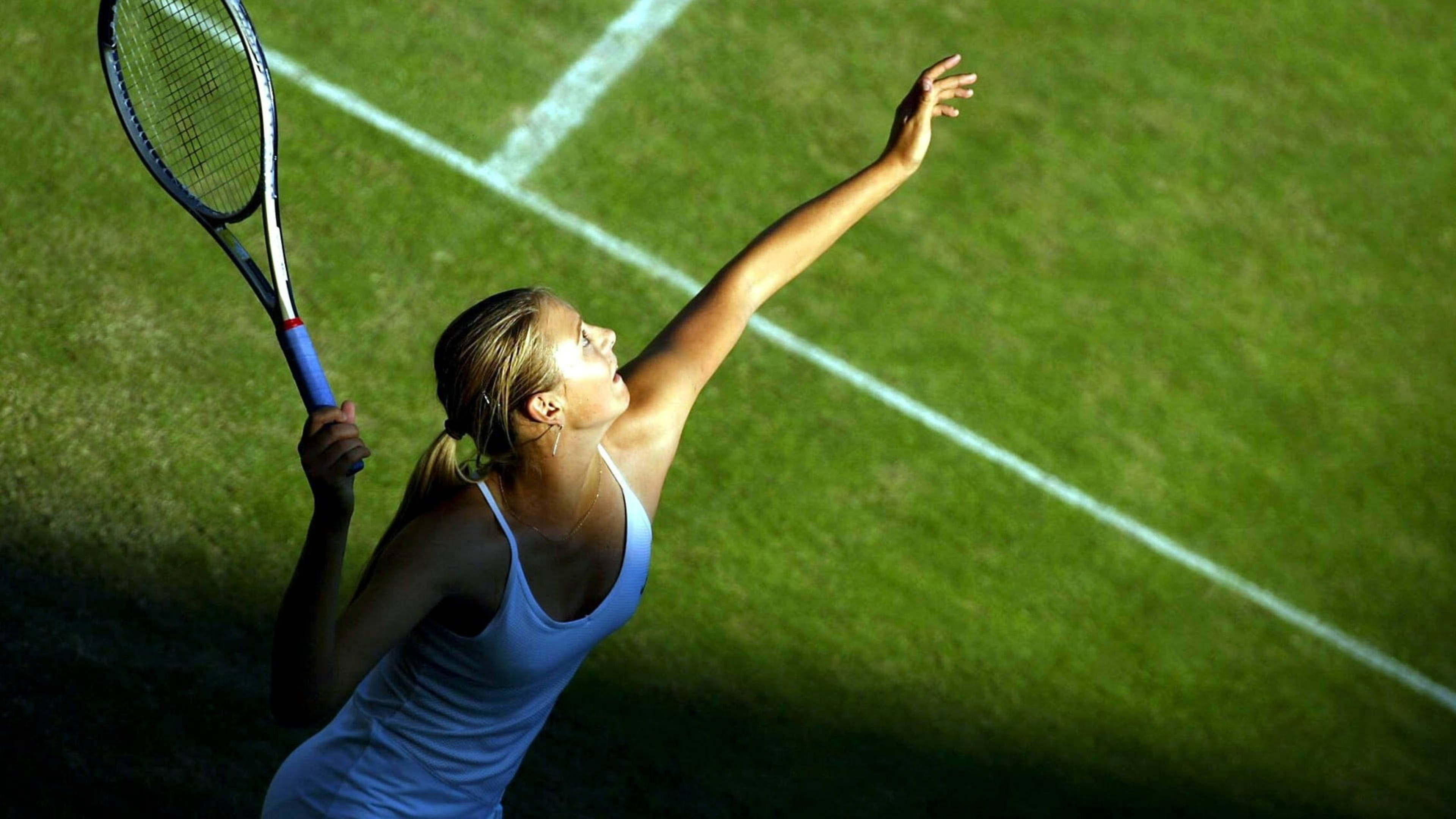 Maria Sharapova 桌布 壁紙 — 一位身穿白色背心的女網球運動員在明亮的體育場燈光下於綠色草地場上發球。