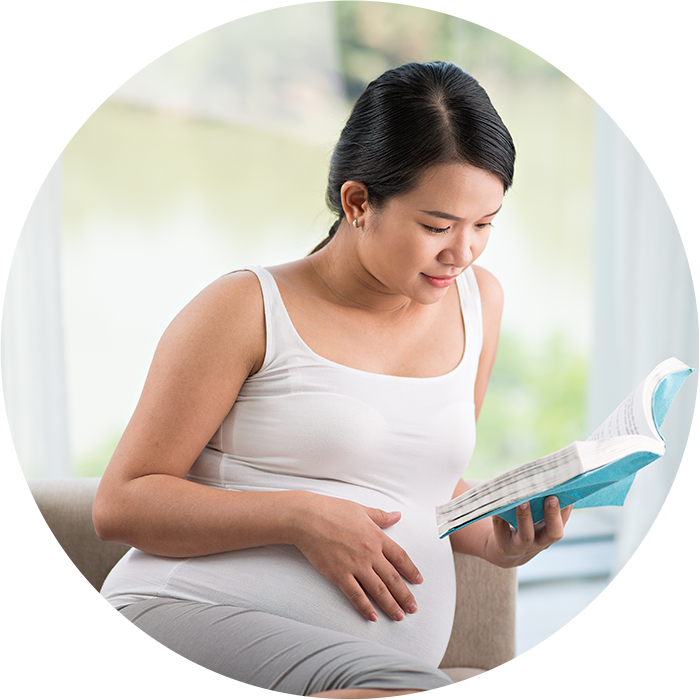 Reading 桌布 壁紙 — 一位身穿白色背心的孕婦平靜地坐在米色沙發上，輕輕將一隻手放在肚子上，同時閱讀一本藍色的書。