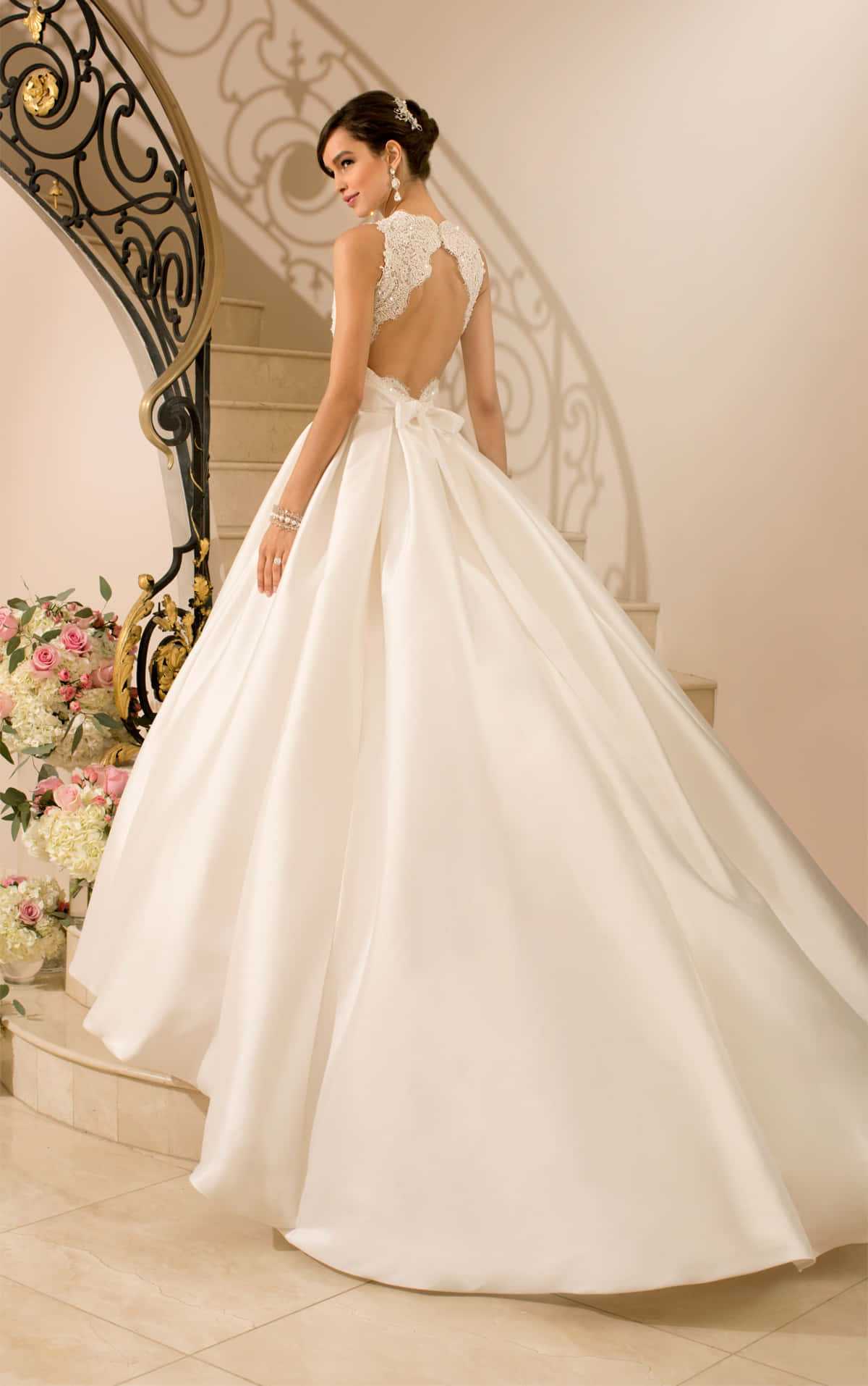 Wedding Gown 桌布 壁紙 — 一位身穿白色舞會禮服、背部有蕾絲設計的新娘，優雅地站在大理石樓梯上，旁邊是花卉佈置。