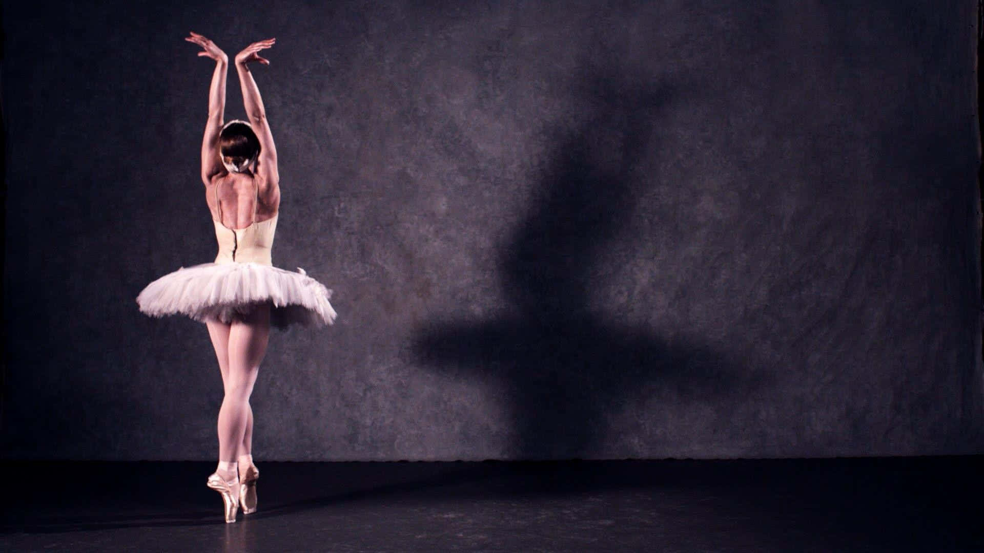 Ballet Dancer 桌布 壁紙 — 一位身穿白色芭蕾舞裙的芭蕾舞者，在深色紋理背景前踮起腳尖，雙臂高舉，投下戲劇性的陰影。