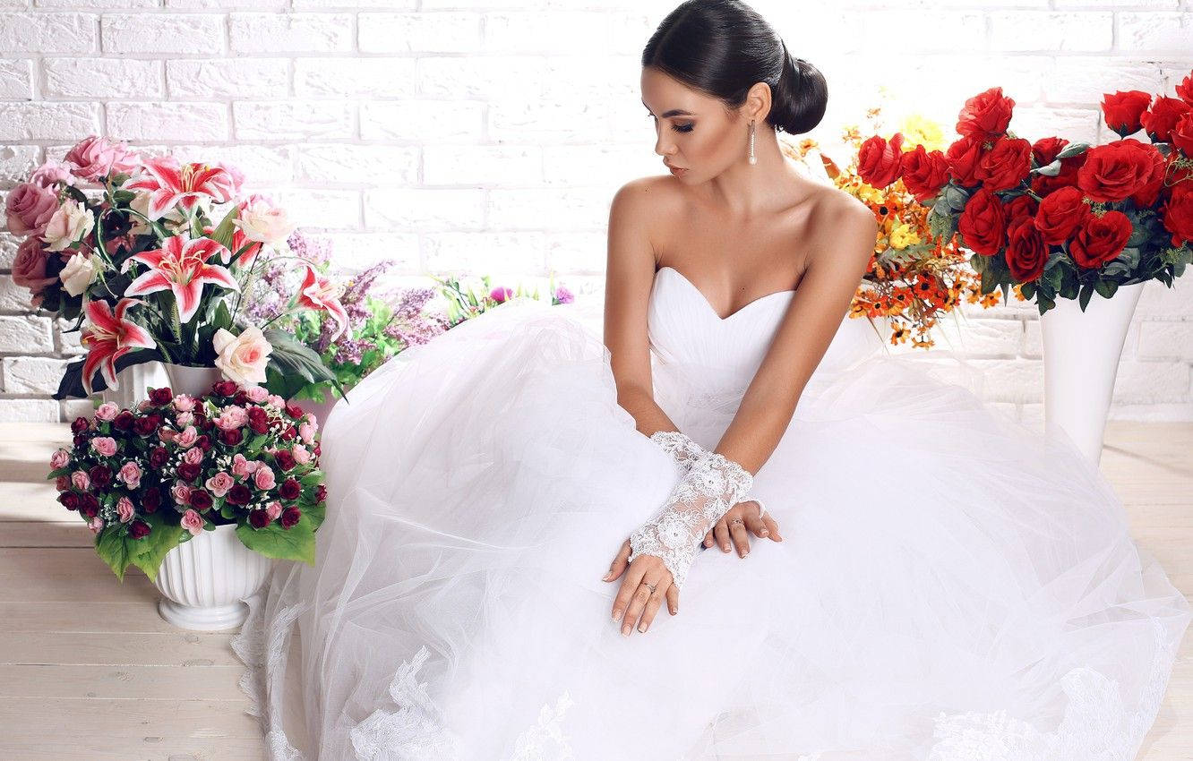 Bride 桌布 壁紙 — 一位身穿白色蓬鬆婚紗的新娘，優雅地坐在白色磚牆前，旁邊是色彩鮮豔的花藝佈置。