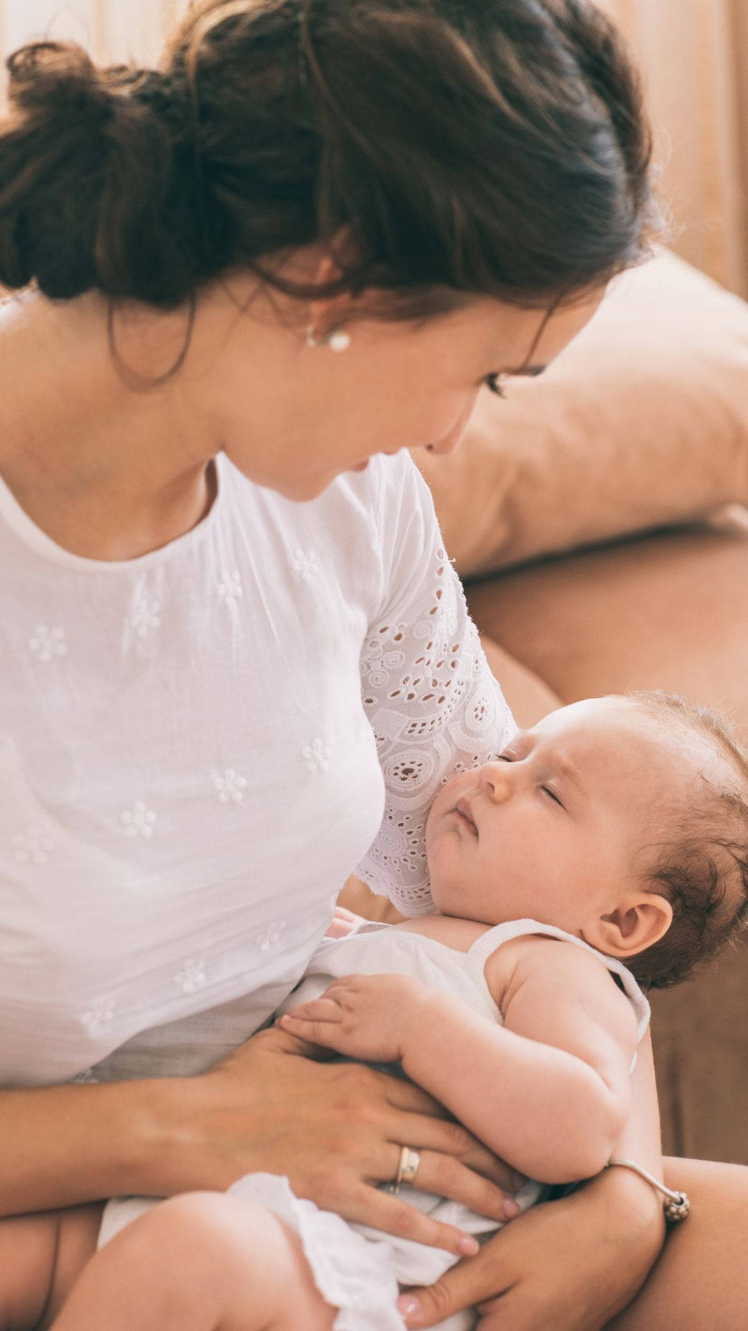 Mom 桌布 壁紙 — 一位身穿白色蕾絲上衣的母親，在柔軟的沙發上輕輕抱著她熟睡的嬰兒，溫柔的時刻。