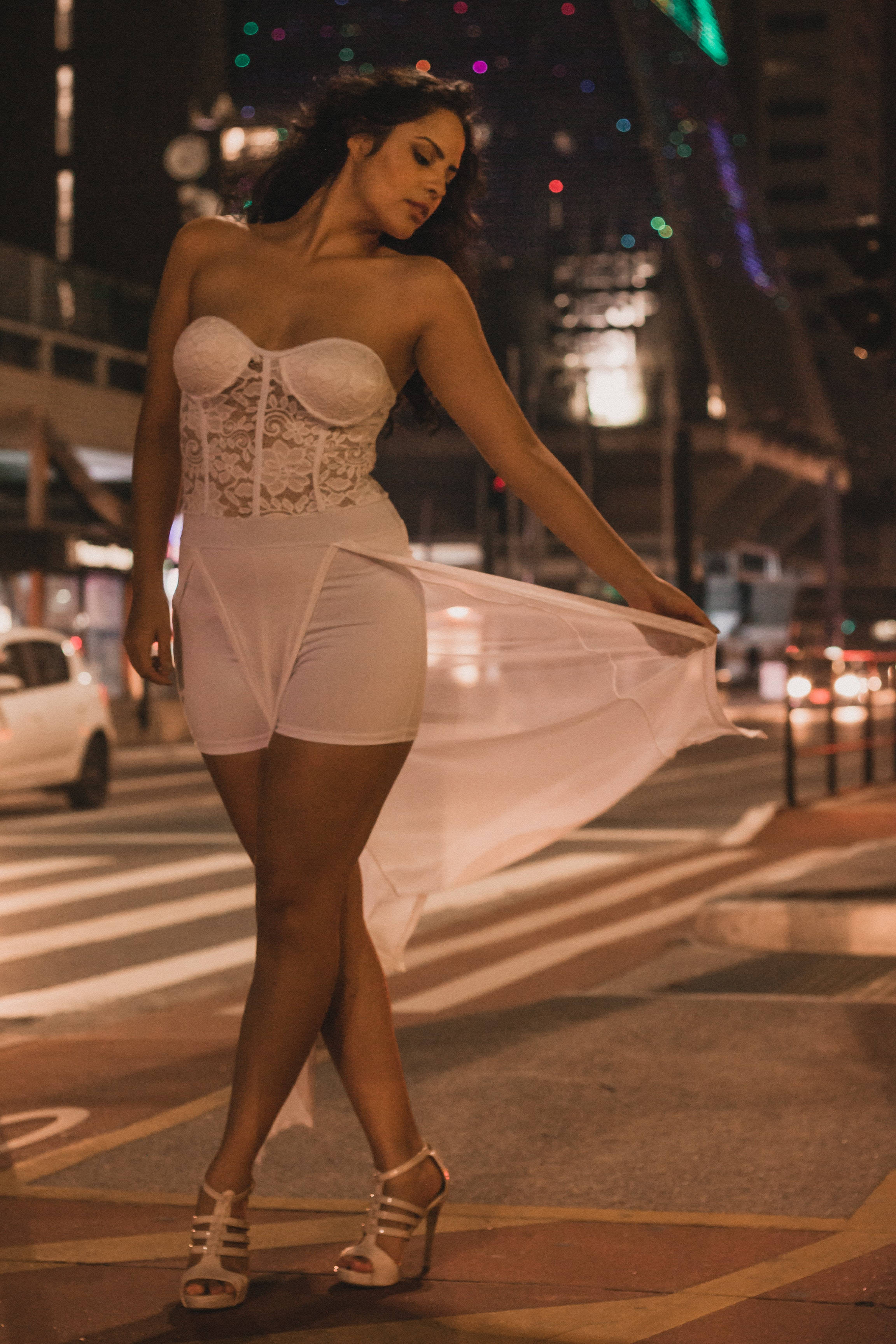 Sensual 桌布 壁紙 — 一位身穿白色蕾絲內衣和短褲的女性在夜晚的城市街道上擺姿勢，手持飄逸布料，背後霓虹燈光模糊。