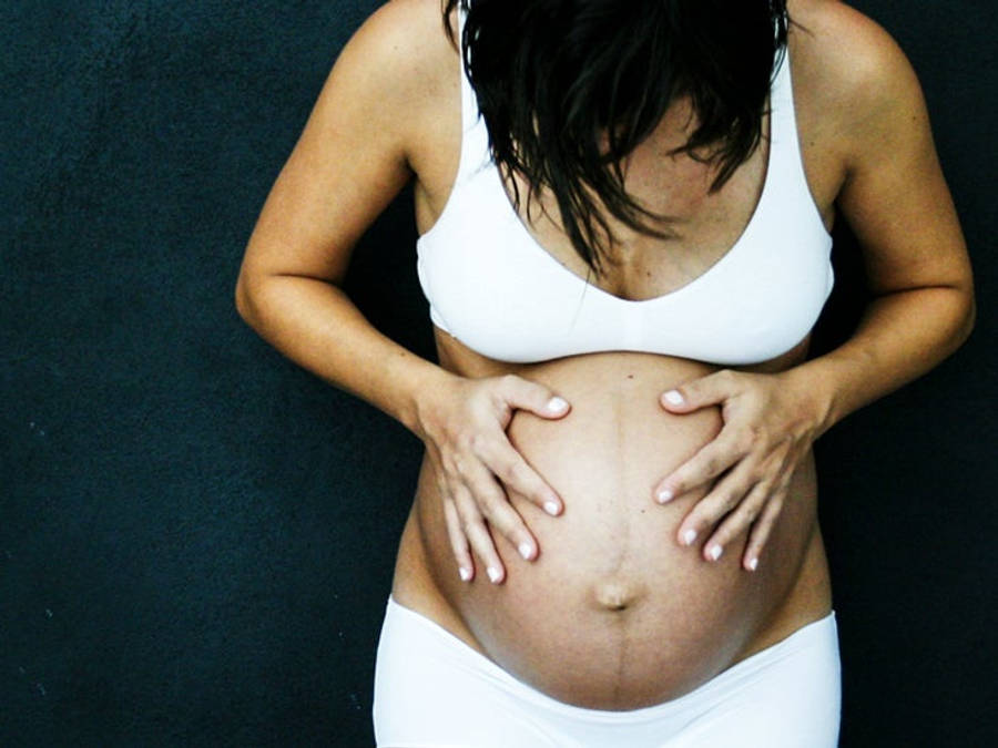 Pregnant 桌布 壁紙 — 一位身穿白色蕾絲內衣的孕婦，在深色紋理背景前輕柔地抱著她的肚子。