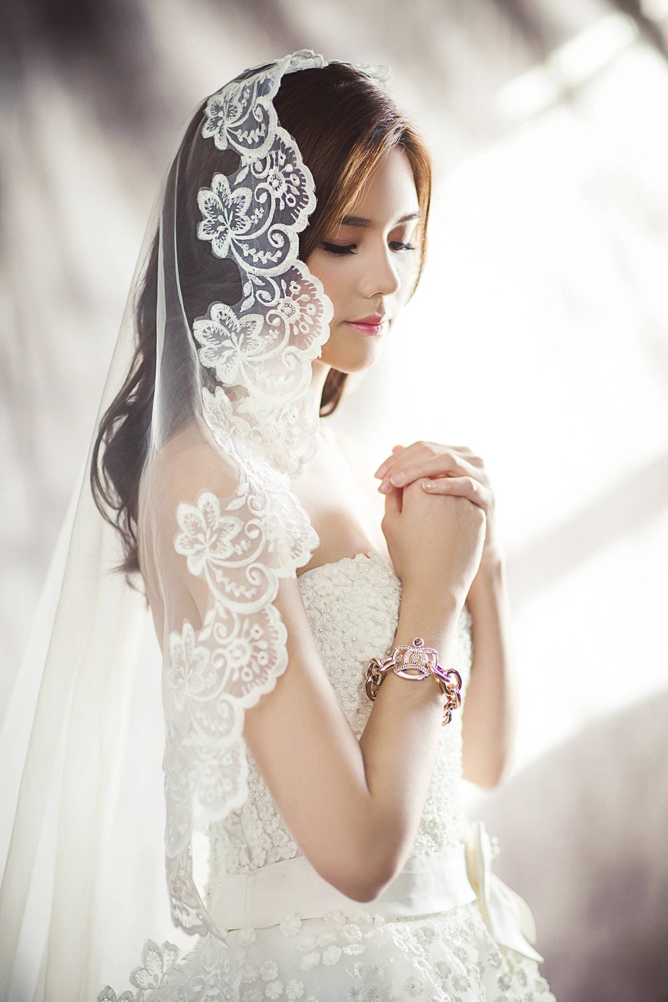 美女 桌布 壁紙 — 一位身穿白色蕾絲婚紗和頭紗的新娘在柔和窗光下合十祈禱。