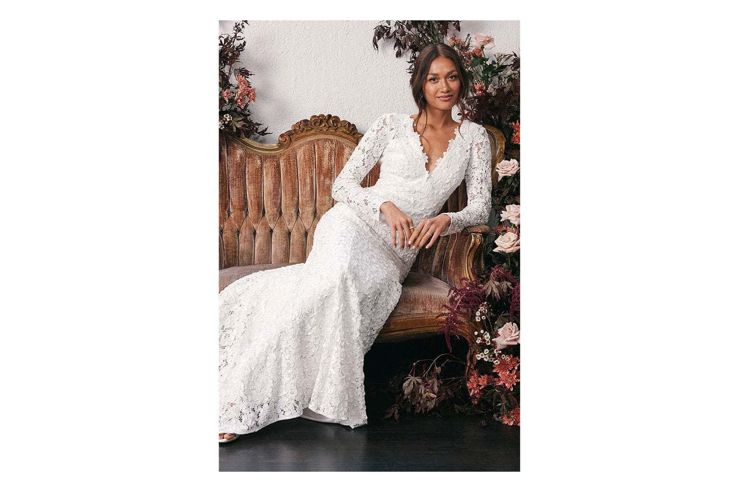 Bride 桌布 壁紙 — 一位身穿白色蕾絲婚紗的女性優雅地坐在一張裝飾華麗的木長椅上，周圍環繞著茂盛的花藝佈置。