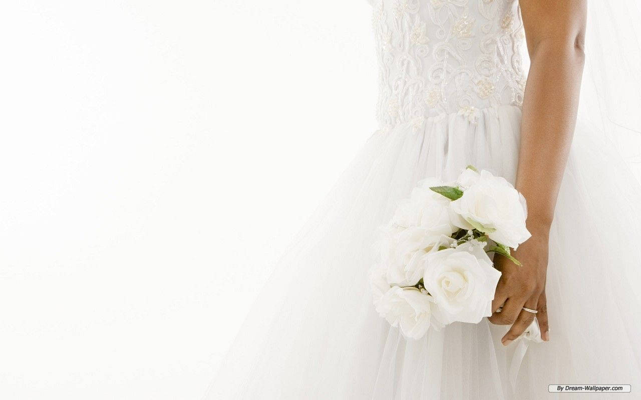 Bride 桌布 壁紙 — 一位身穿白色蕾絲婚紗的新娘，在明亮的白色背景前手持一束白玫瑰。
