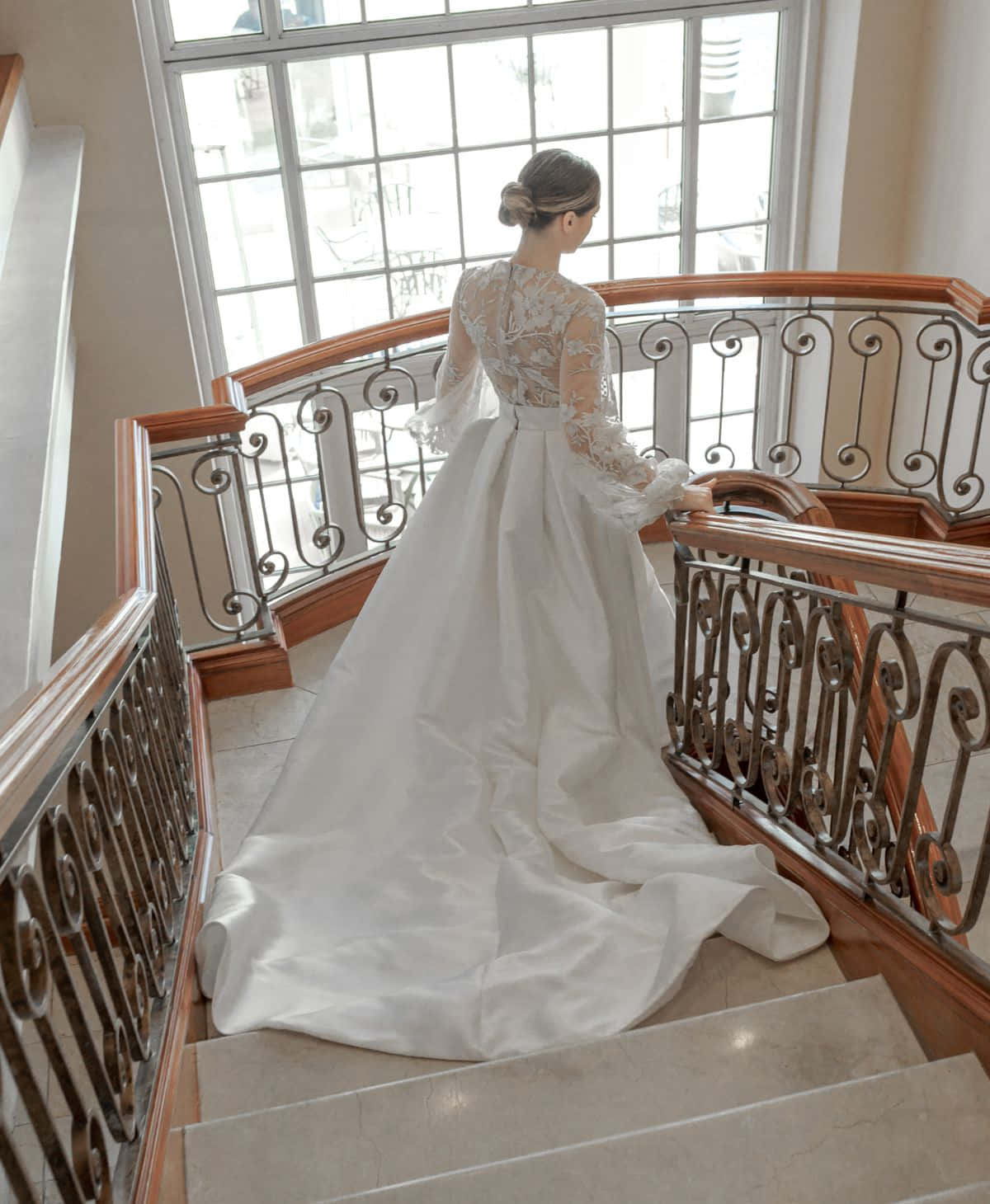 Bride's Dress 桌布 壁紙 — 一位身穿白色蕾絲婚紗的新娘，在柔和自然光線的沐浴下，沿著帶有華麗鐵藝欄杆的大樓梯走下。