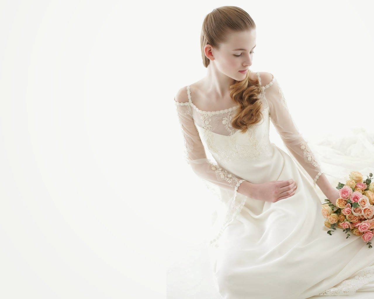 Bride 桌布 壁紙 — 一位身穿白色蕾絲禮服的新娘優雅地跪著，手持一束柔和的粉紅和蜜桃色玫瑰，背景是明亮的白色。