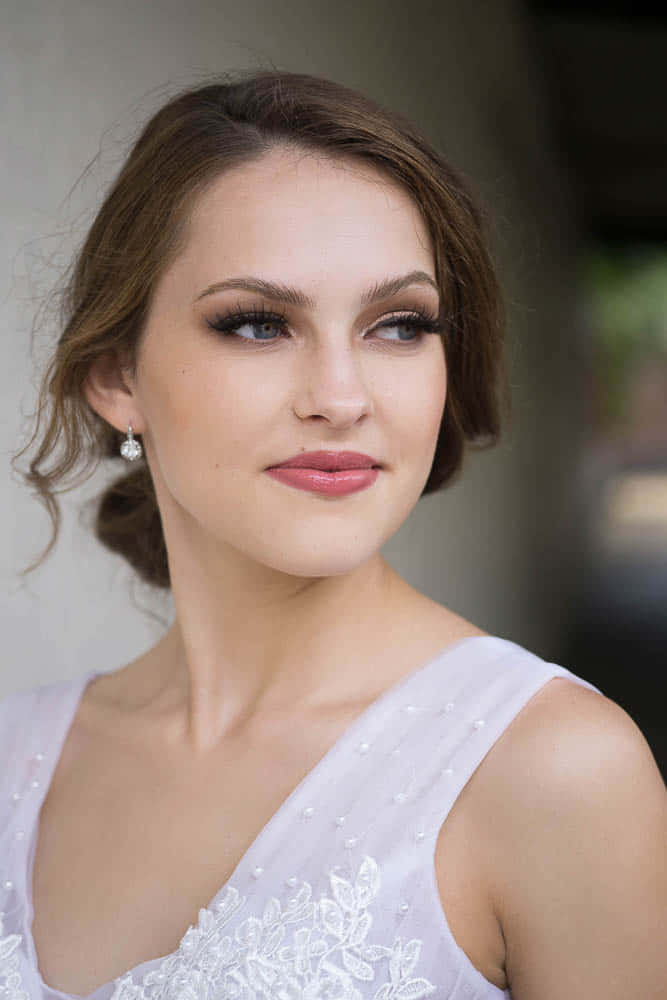 Bridal Makeup 桌布 壁紙 — 一位身穿白色蕾絲連衣裙、綴有珍珠細節的新娘，溫柔地望向一旁，她的頭髮梳成優雅的捲髮。