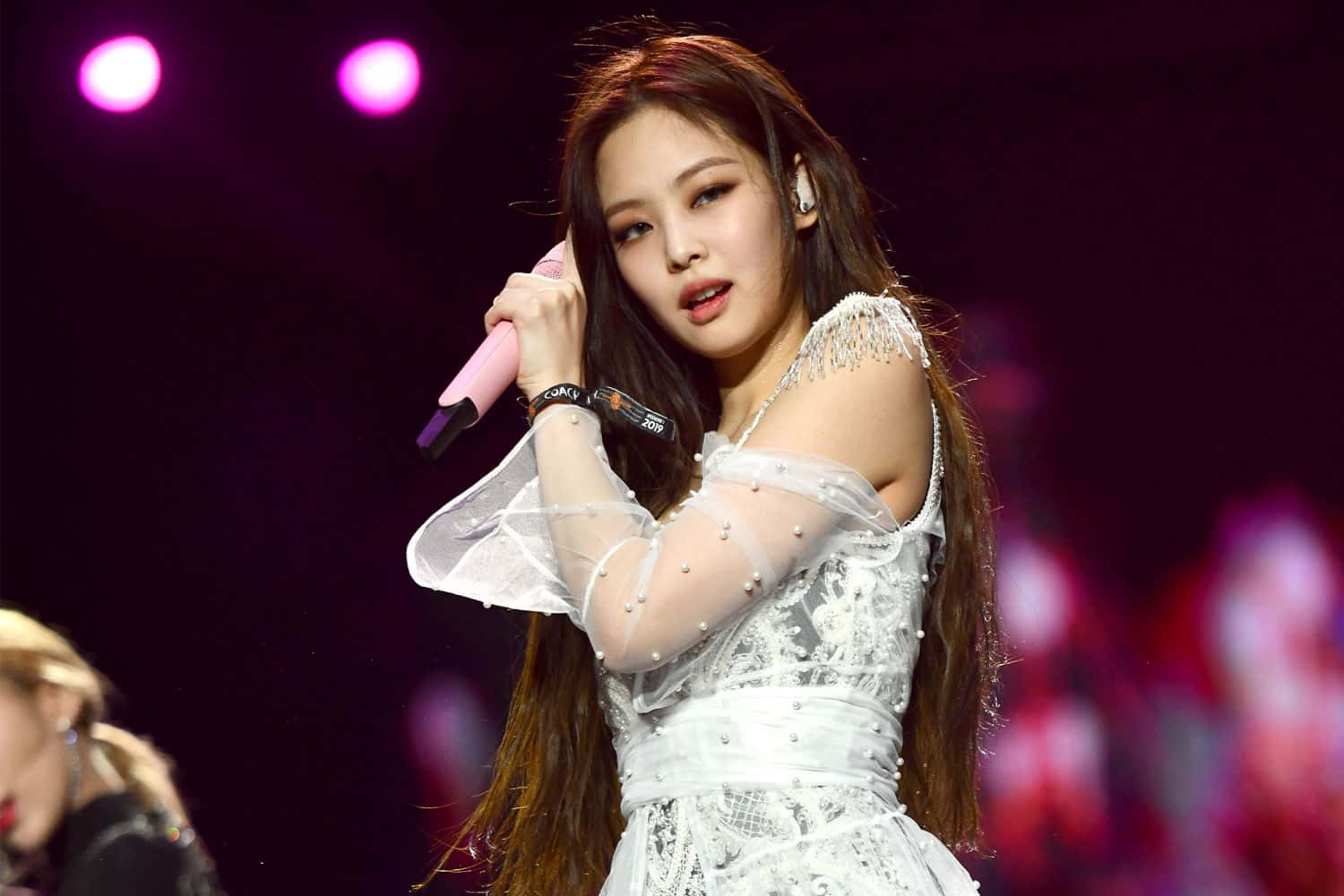 BLACKPINK 桌布 壁紙 — 一位身穿白色蕾絲連衣裙的女歌手在粉紅色聚光燈下拿著粉紅色麥克風在舞台上表演。