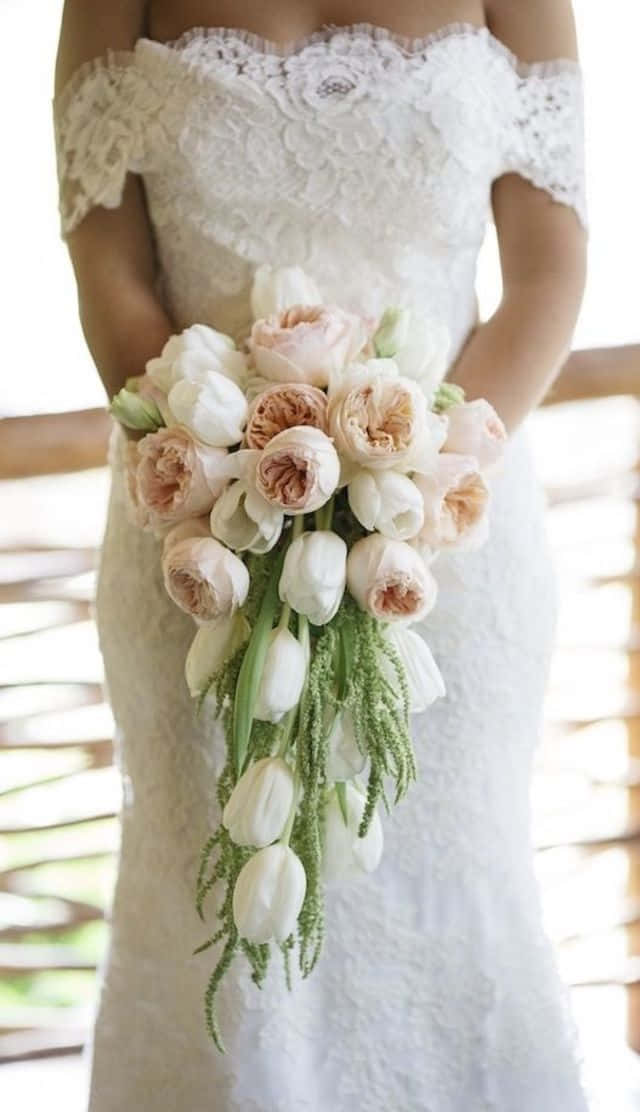 鬱金香 桌布 壁紙 — 一位身穿白色蕾絲露肩婚紗的新娘，手持一束由淡粉和白色牡丹及鬱金香組成的瀑布式花束。