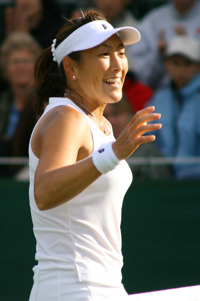 Tennis 桌布 壁紙 — 一位身穿白色裝備、面帶微笑的女網球手在明亮的日光下於草地場上向觀眾揮手。