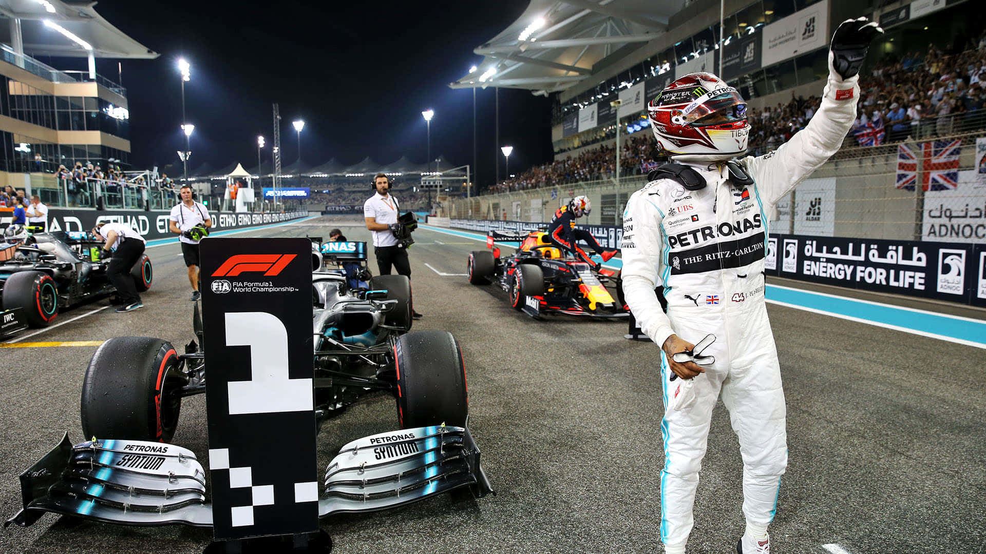 Formula One 桌布 壁紙 — 一位身穿白色裝備的F1車手在夜間與他的賽車在方格旗和頒獎台旁慶祝勝利。