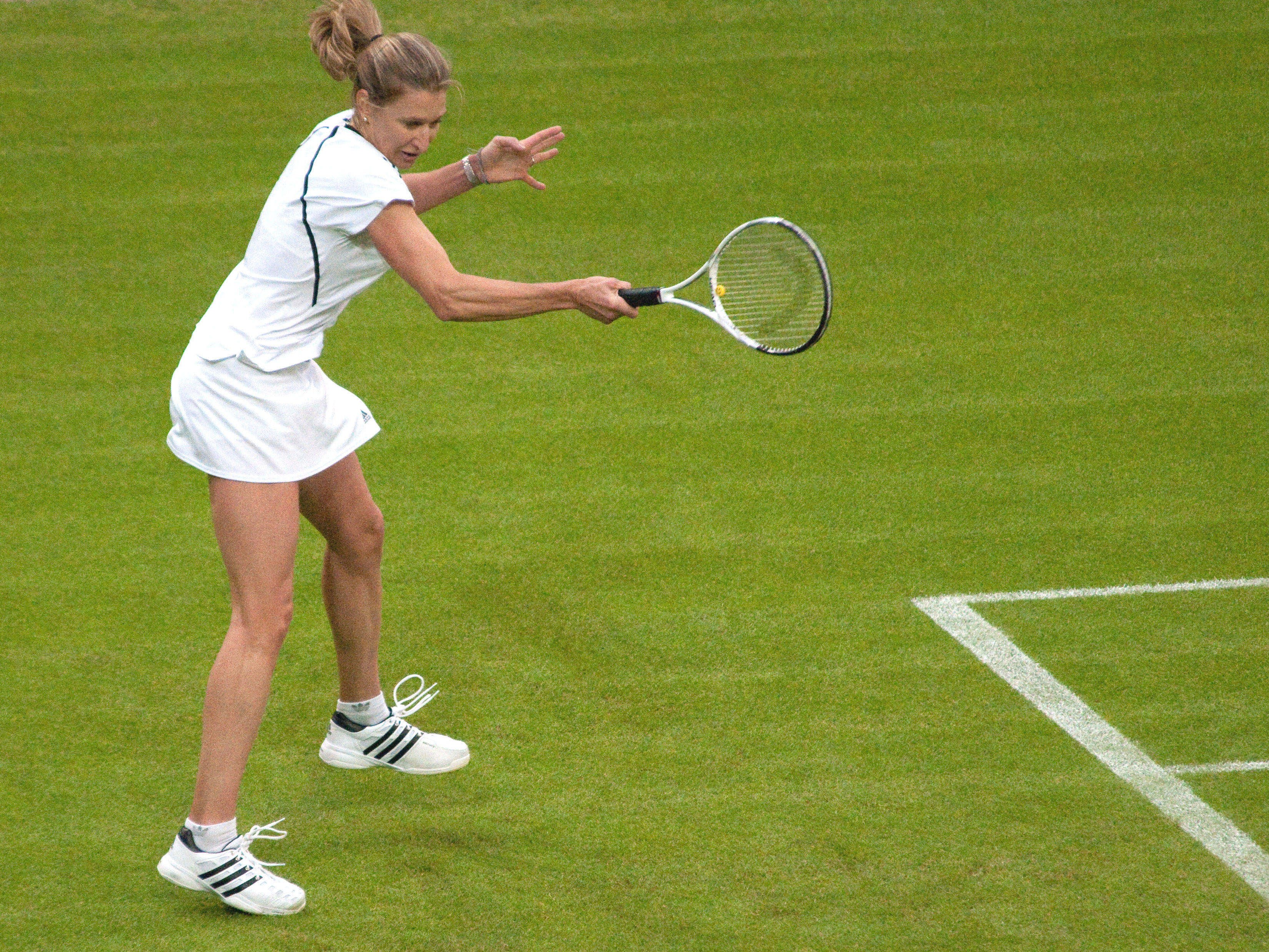 Tennis 桌布 壁紙 — 一位身穿白色裝備的女網球運動員在草地上專注地揮動球拍。