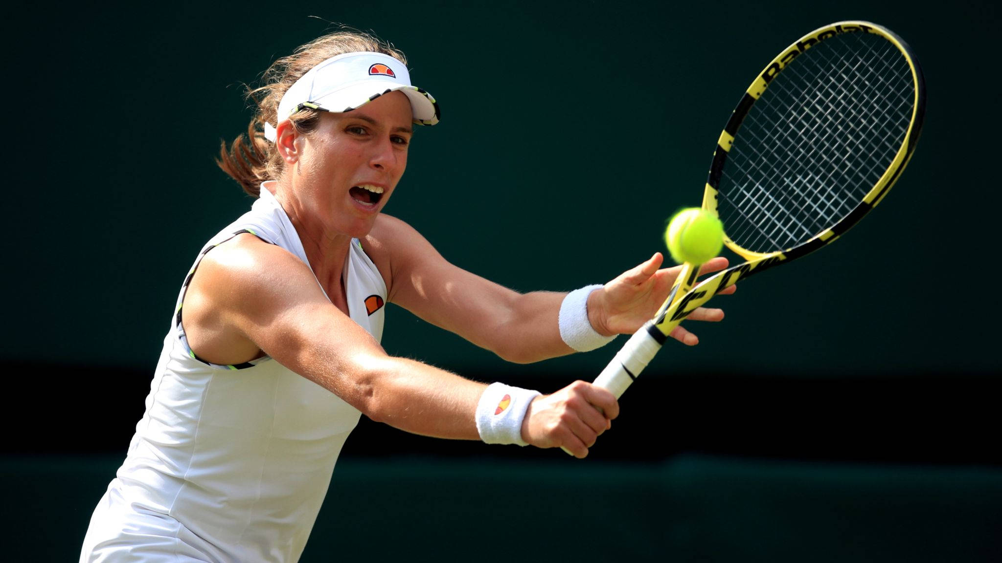 Athletic 桌布 壁紙 — 一位身穿白色裝備的女網球選手向前衝刺，用黃黑相間的球拍擊打一顆亮黃色的球，背景為深綠色。
