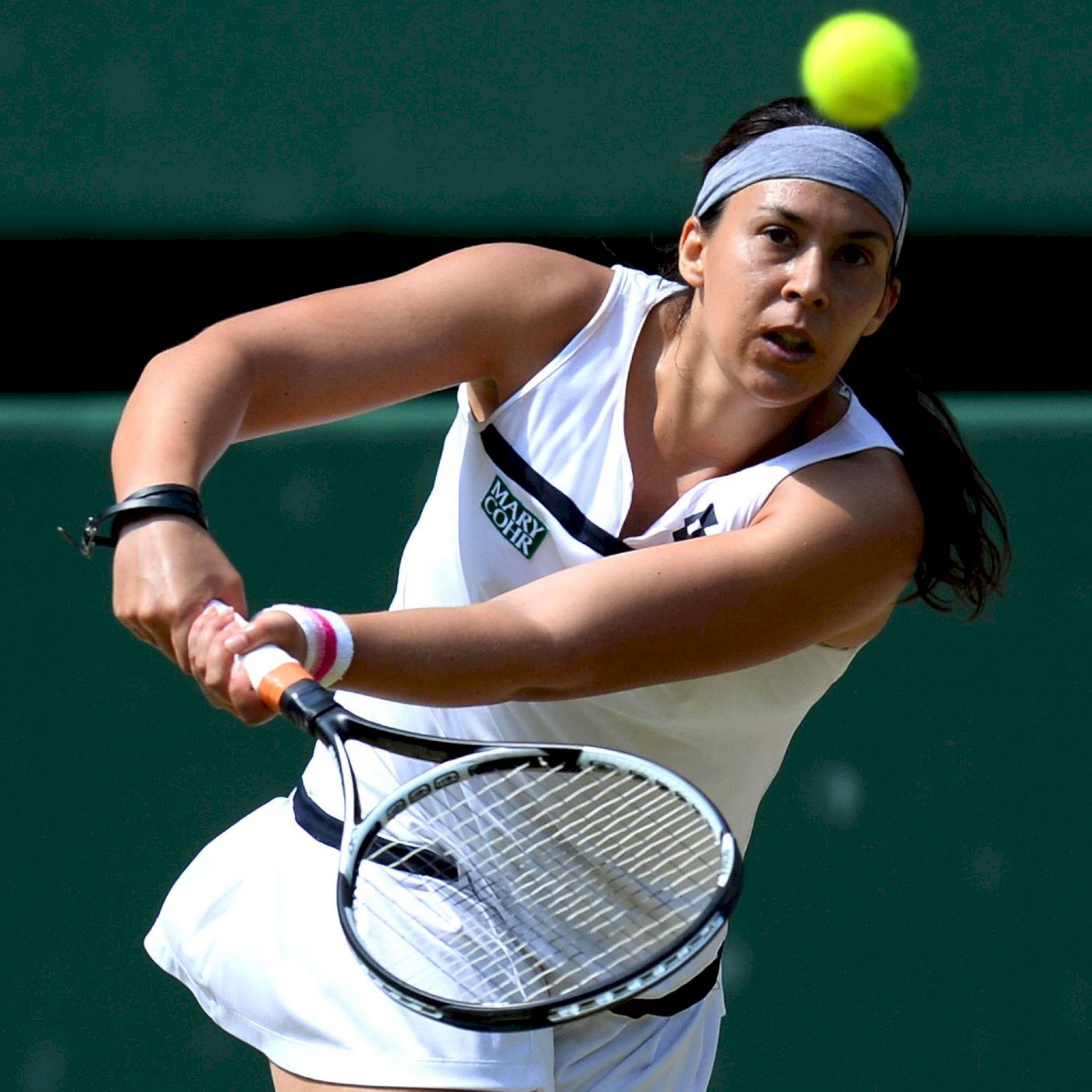運動 桌布 壁紙 — 一位身穿白色裝備的女網球選手在綠色球場背景下揮拍擊打一個亮黃色的球。