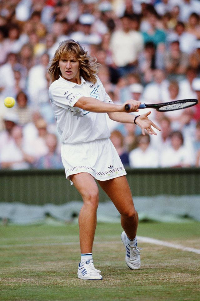 Tennis 桌布 壁紙 — 一位身穿白色裝備的女網球選手在草地場上揮拍擊打黃色球，身後有模糊的觀眾。
