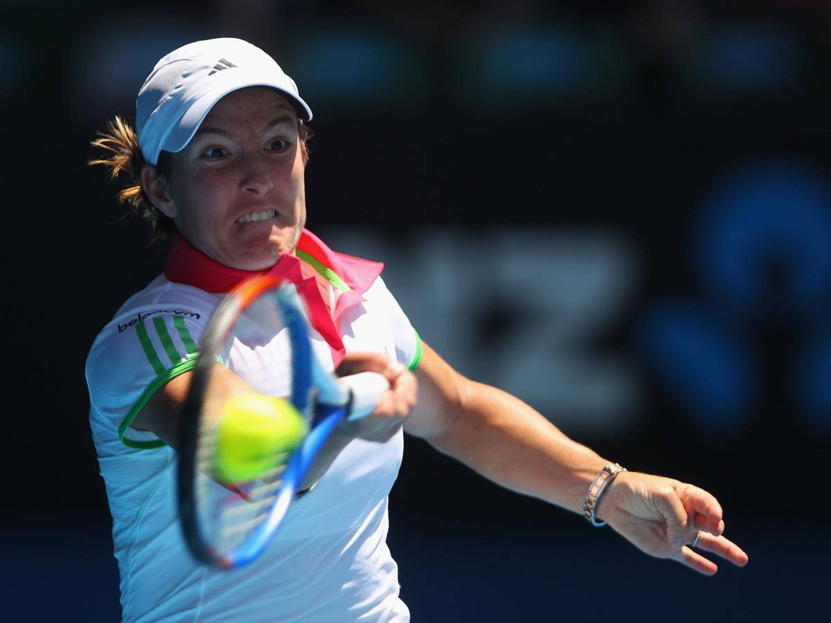 Australian Open 桌布 壁紙 — 一位身穿白色裝備的女網球選手在體育館燈光下猛烈揮拍擊向一個亮黃色的球。