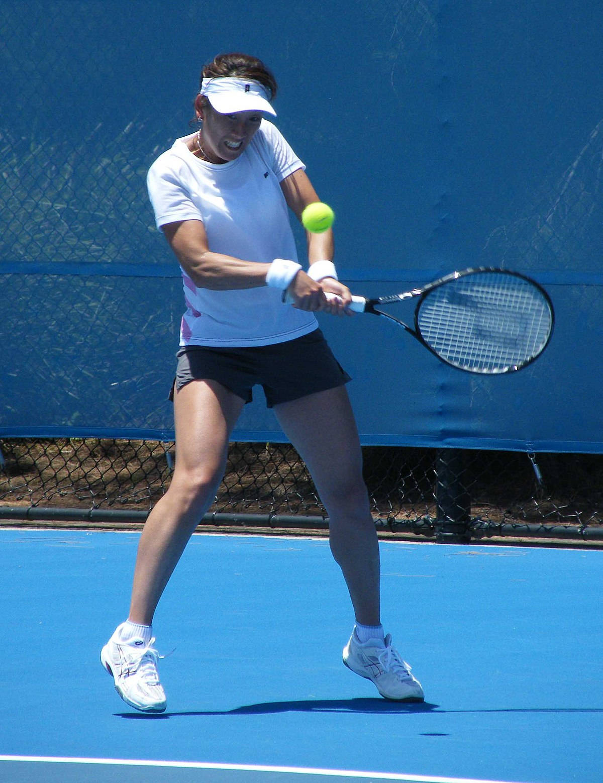 Athlete 桌布 壁紙 — 一位身穿白色裝備的女網球選手在鮮藍色球場上揮拍擊打亮黃色的球。