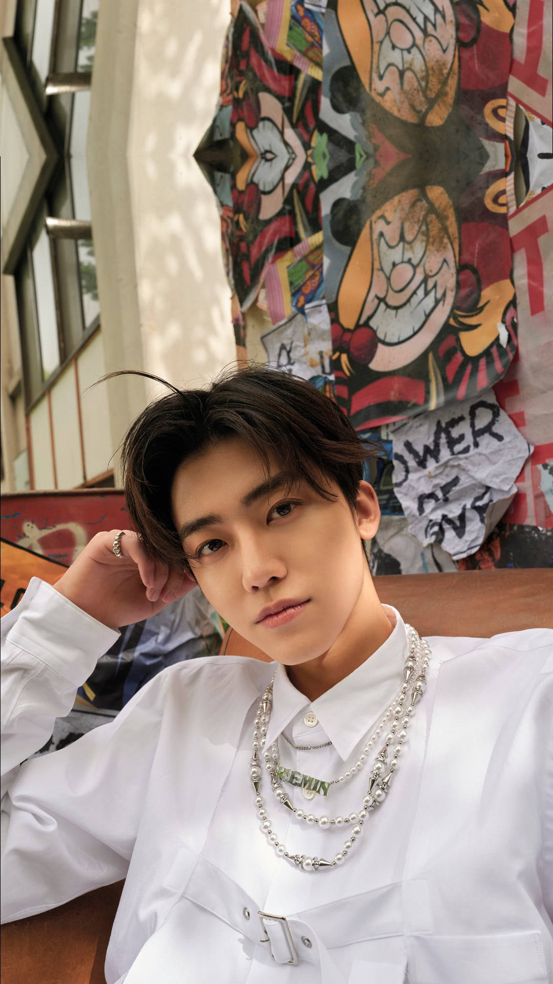 jaemin 桌布 壁紙 — 一位身穿白色襯衫和層疊銀鍊的年輕男子，在色彩繽紛的卡通臉塗鴉牆前擺姿勢。