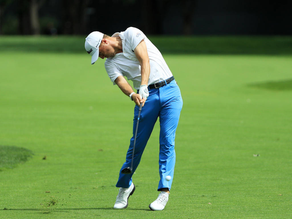 Golf Club 桌布 壁紙 — 一位身穿白色襯衫和藍色褲子的高爾夫球手在晴朗的日光下，在明亮的綠色球道上揮桿。