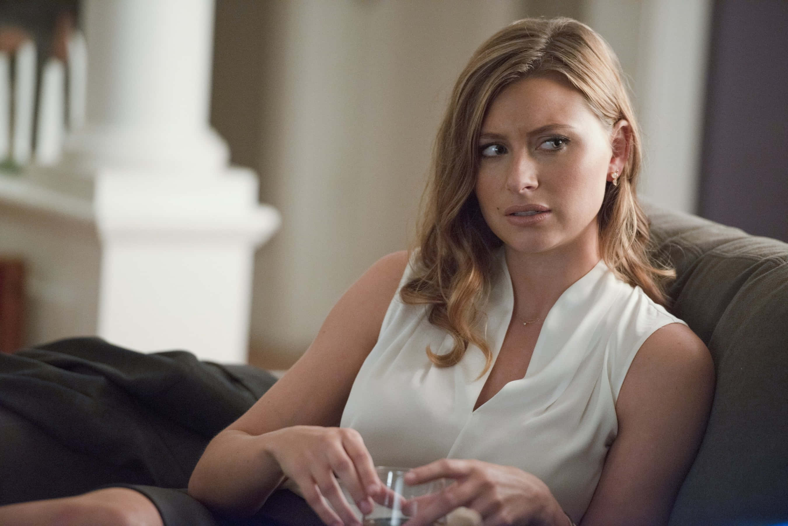 aly michalka 桌布 壁紙 — 一位身穿白色襯衫的女士坐在沙發上，拿著一個杯子，表情憂慮。