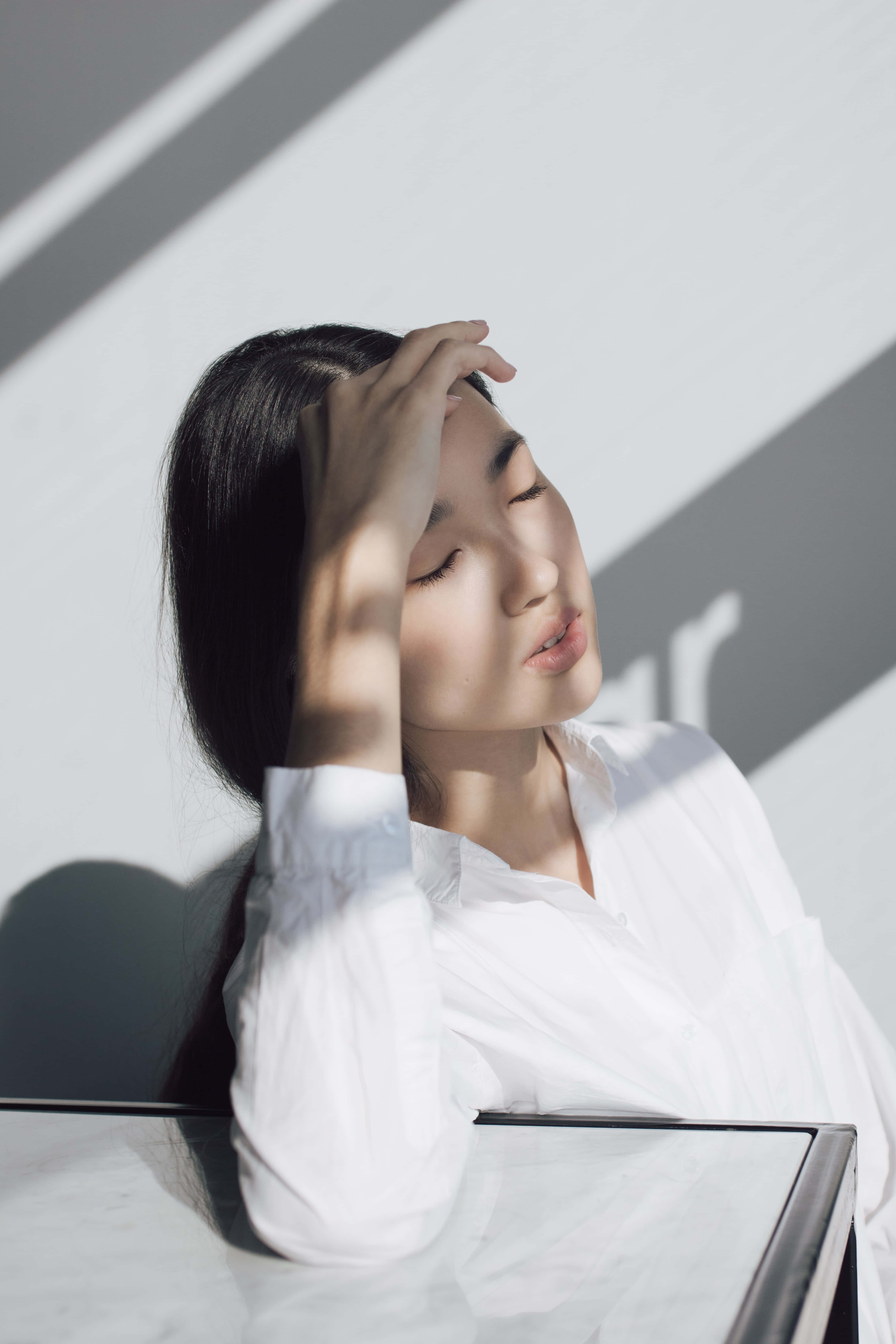 Frustrated 桌布 壁紙 — 一位身穿白色襯衫的女性將頭靠在牆上，陽光在她臉上和下方表面投射出銳利的幾何陰影。