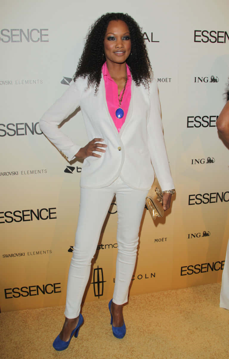 Garcelle Beauvais 桌布 壁紙 — 一位身穿白色西裝和亮粉色襯衫的女性在Essence Awards活動的金色地毯上自信地擺姿勢。