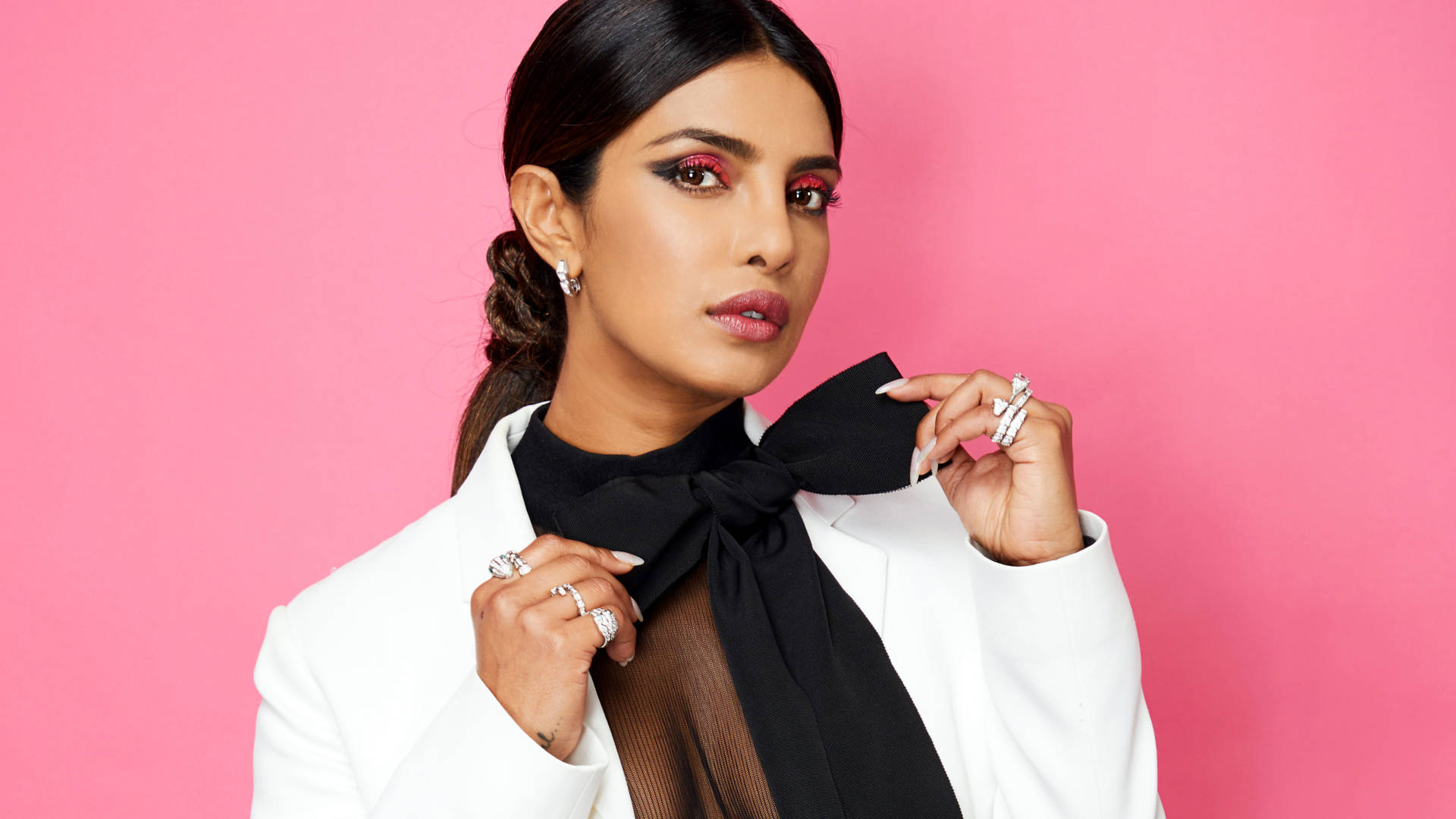 Priyanka 桌布 壁紙 — 一位身穿白色西裝外套和黑色蝴蝶結領帶的自信女性，在充滿活力的粉紅色背景前自信地擺姿勢。