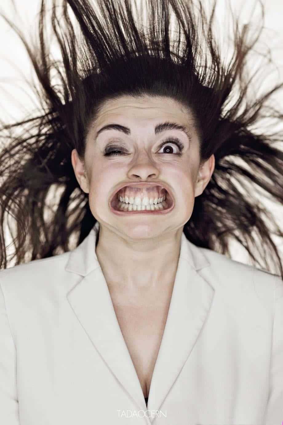 搞笑 桌布 壁紙 — 一位身穿白色西裝外套的女性，深色頭髮向上飛揚，在純色背景前狂笑。
