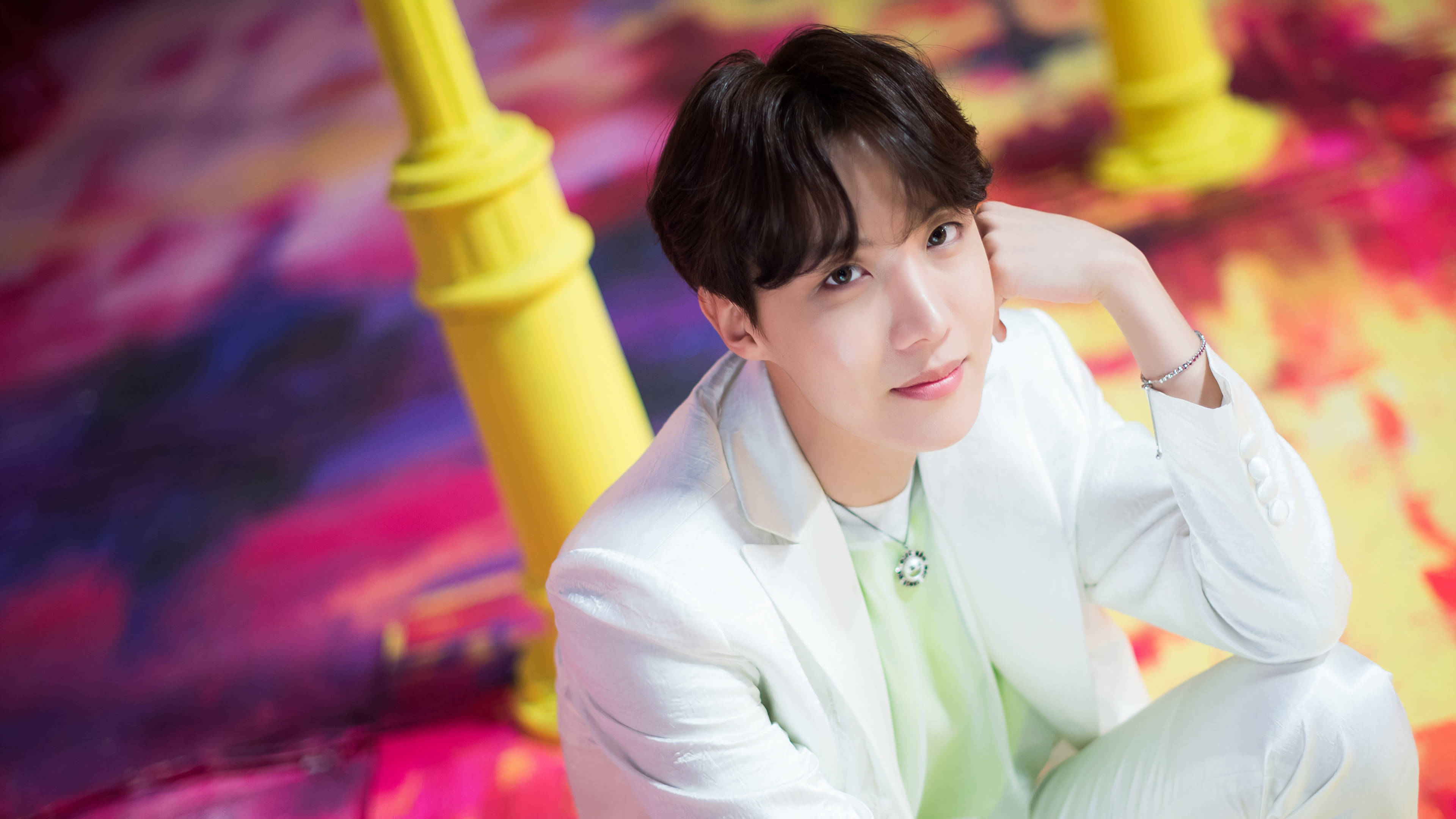 jhope 桌布 壁紙 — 一位身穿白色西裝的年輕男子，在充滿活力的抽象背景前沉思擺姿勢，背景有黃色柱子。