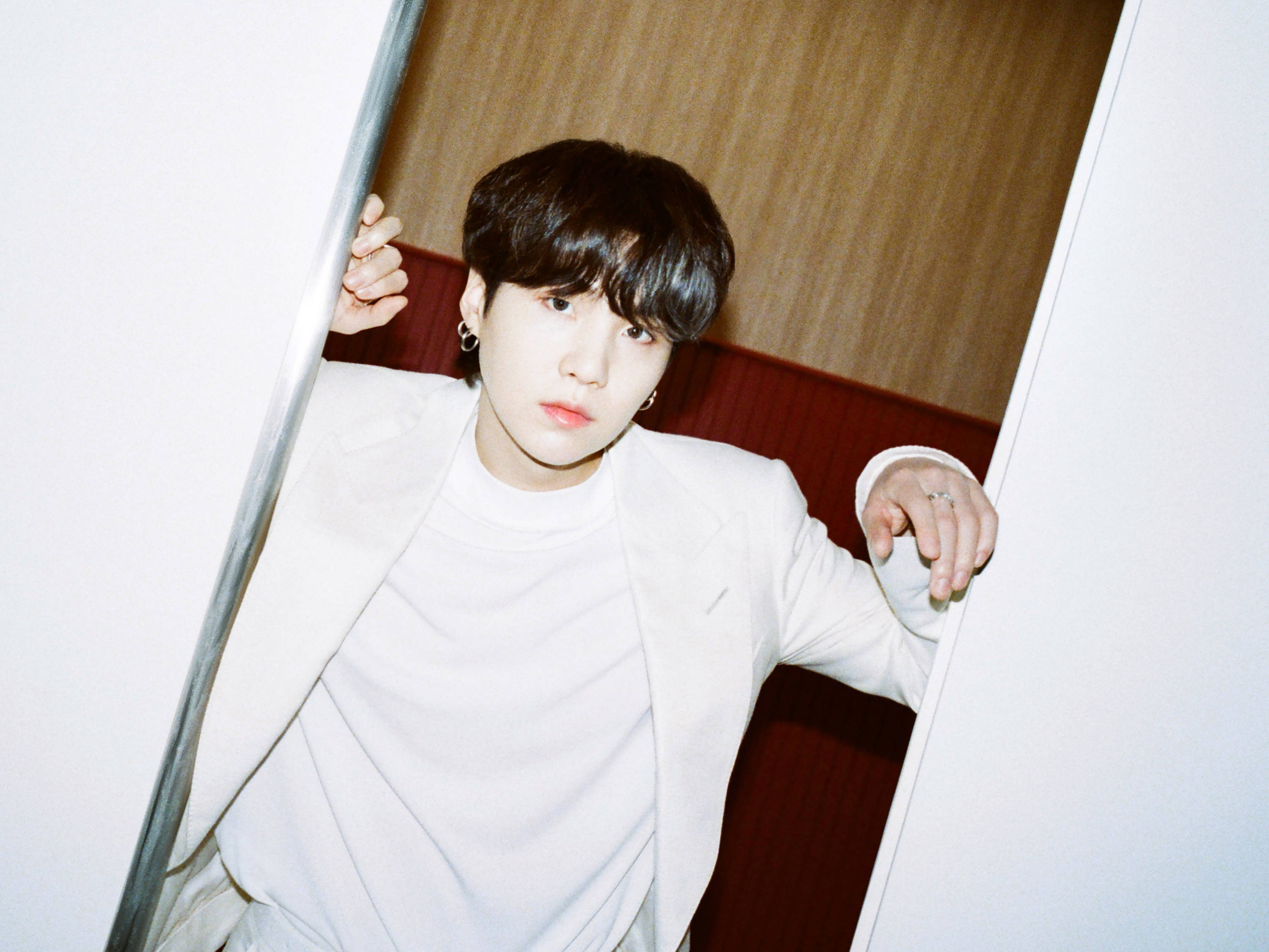 Suga Bts 桌布 壁紙 — 一位身穿白色西裝的年輕男子，神情嚴肅，嘴唇鮮紅，倚在門口。