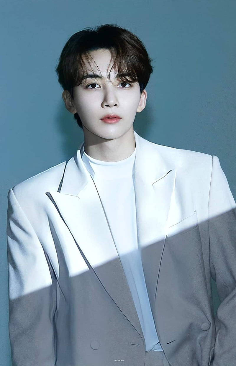 yoon jeonghan 桌布 壁紙 — 一位身穿白色西裝的年輕男子站在清涼的藍色背景前，戲劇性的燈光在他的軀幹上投下銳利的陰影。