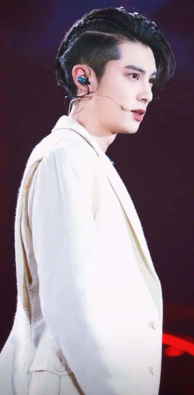 Dylan Wang 桌布 壁紙 — 一位身穿白色西裝的男性表演者站在舞台上，戴著耳機麥克風，在戲劇性的舞台燈光下。