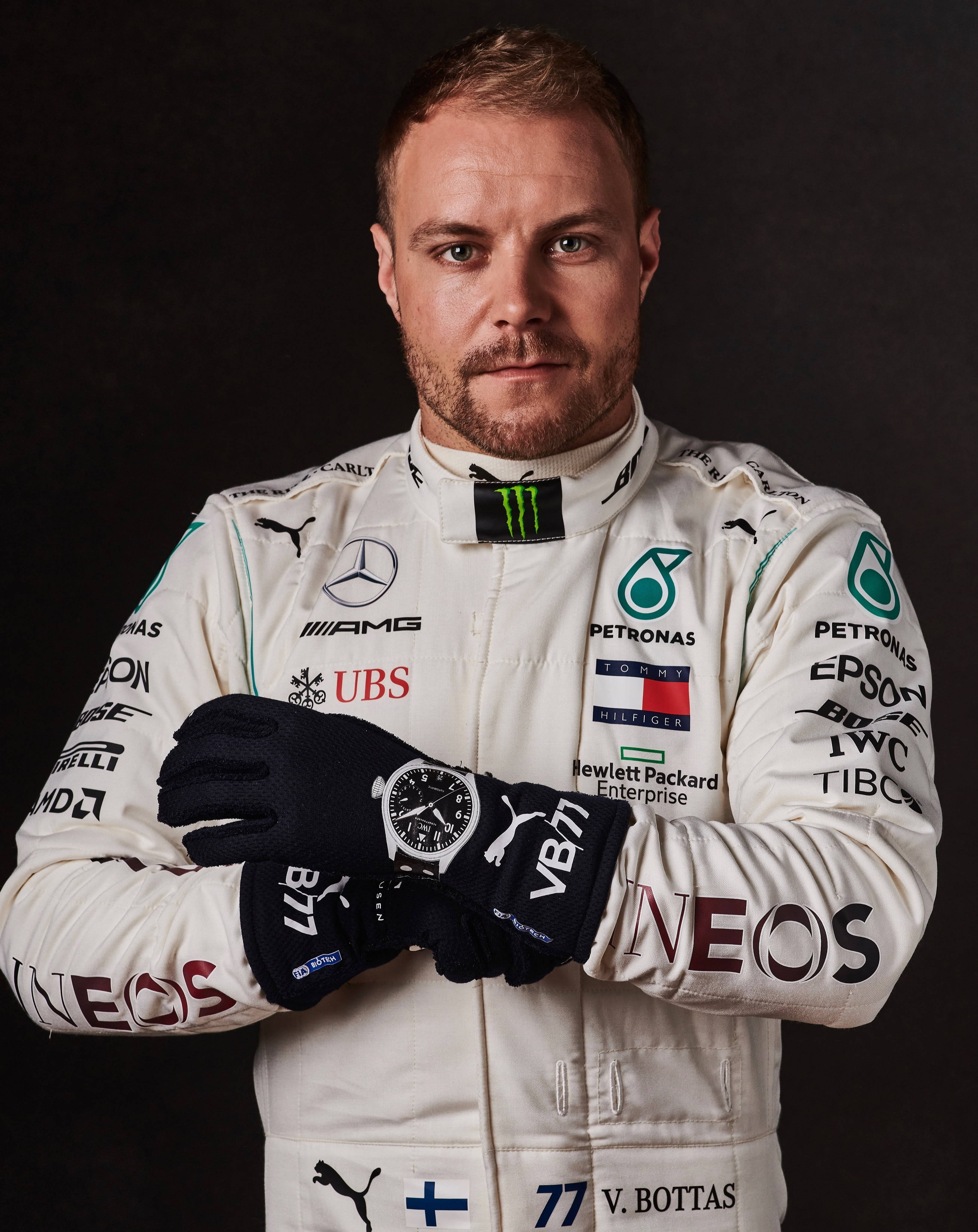 Valtteri Bottas 桌布 壁紙 — 一位身穿白色賽車服、帶有贊助商標誌的F1車手，自信地站在深色背景前。