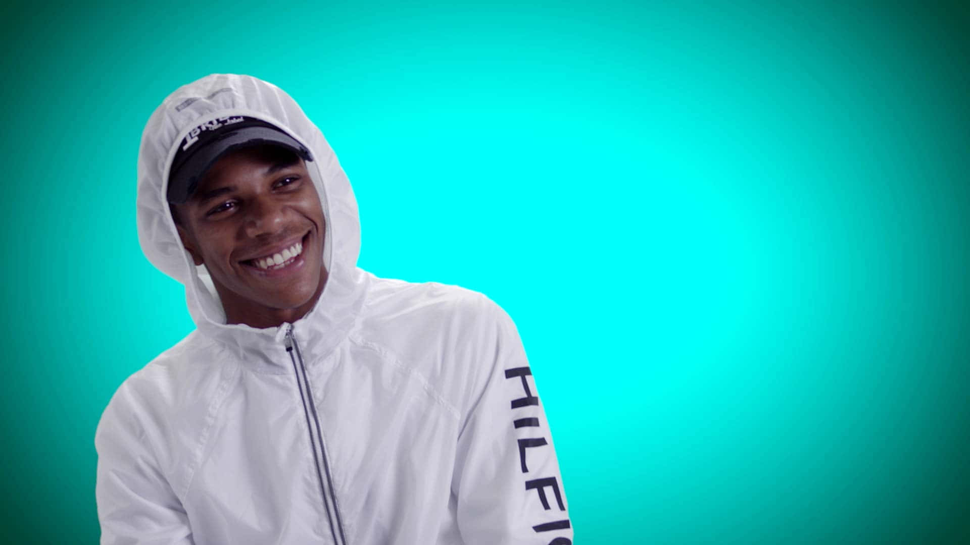 A Boogie Wit Da Hoodie 桌布 壁紙 — 一位身穿白色連帽外套的年輕男子在充滿活力的青綠色漸變背景前燦爛微笑。