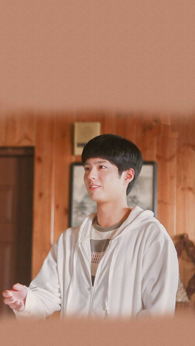 Reply 1988 桌布 壁紙 — 一位身穿白色連帽衫的年輕男子在溫暖光線的木質房間內微笑，牆上掛有裱框藝術品。
